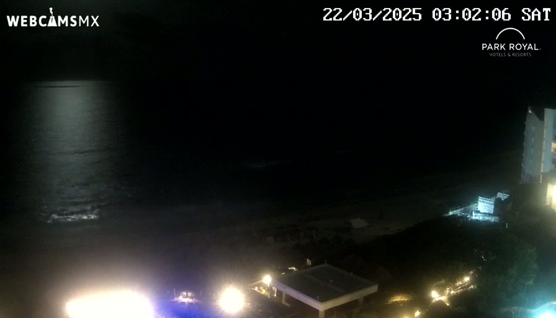A nighttime, moonlit ocean scene is visible from a high vantage point, showing a dark beach and illuminated buildings below.