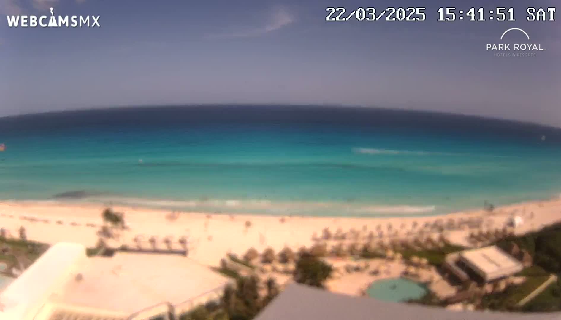 A clear, sunny day reveals a pristine beach with turquoise water,  beach umbrellas, and a resort complex.