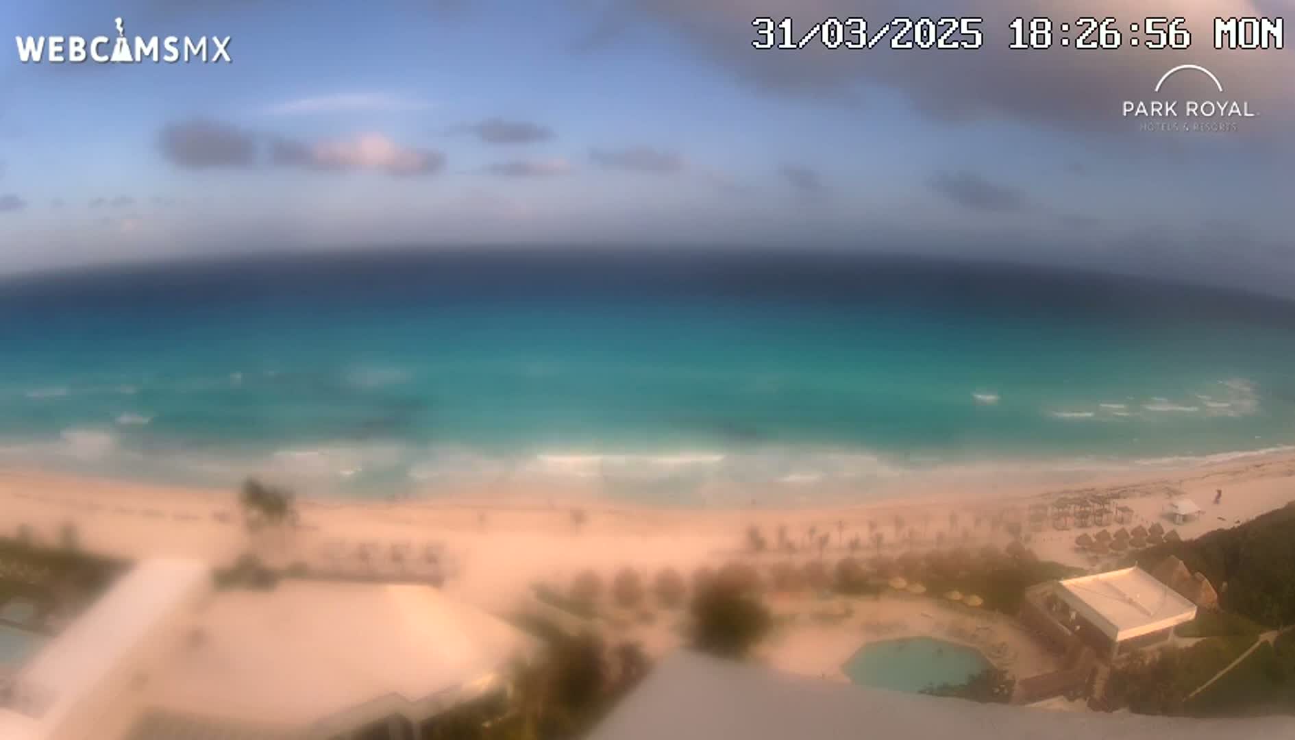 An elevated view shows a beach with turquoise water under a partly cloudy sky.