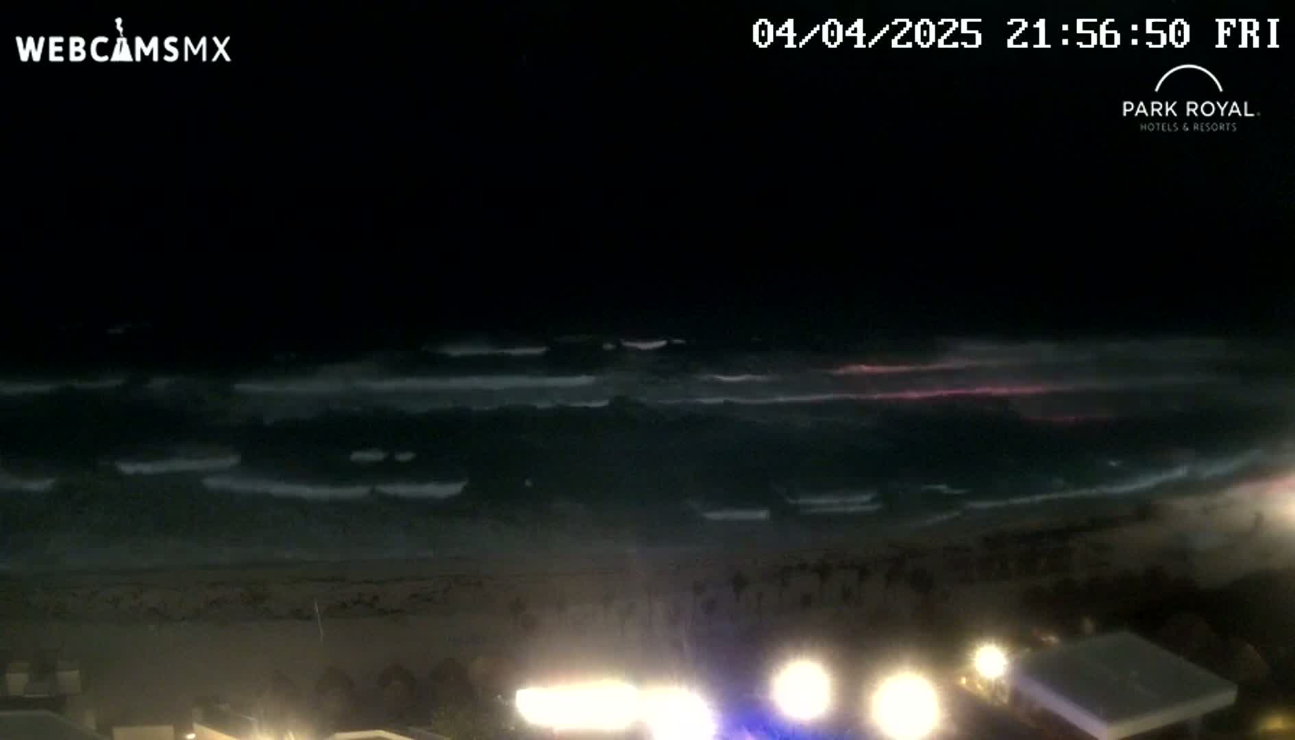 At night, gently rolling waves lap a dark sandy beach under a mostly clear sky with a faint pinkish glow near the horizon.