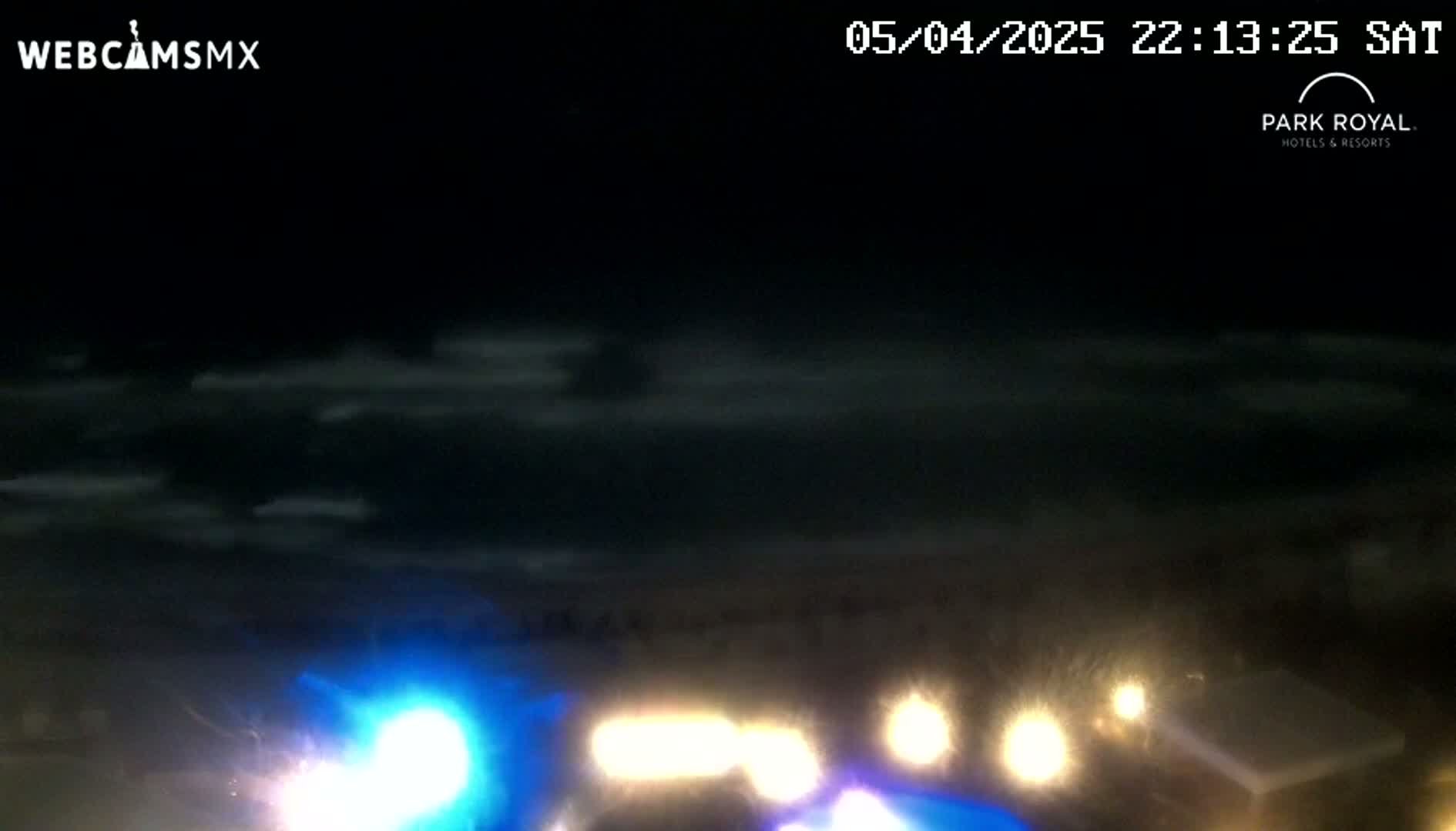 A nighttime view shows a dark sky with thin clouds above dimly lit vehicles and structures.