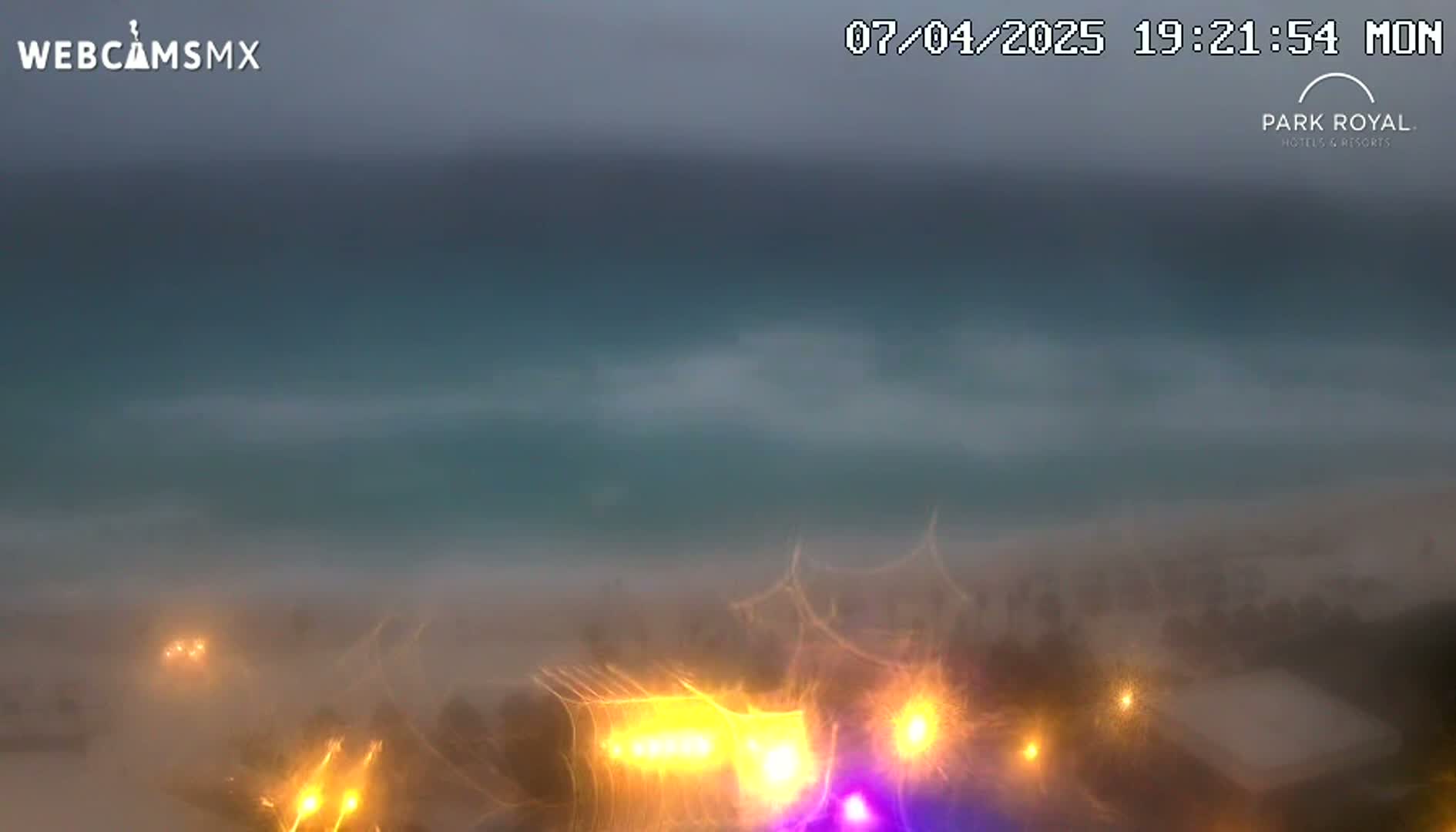A hazy, overcast view of a beach at night, with lights visible from buildings and vehicles in the foreground.
