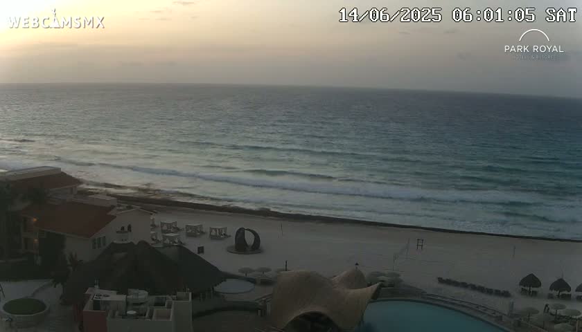 A beachside resort at sunrise with calm ocean waves gently lapping the shore.