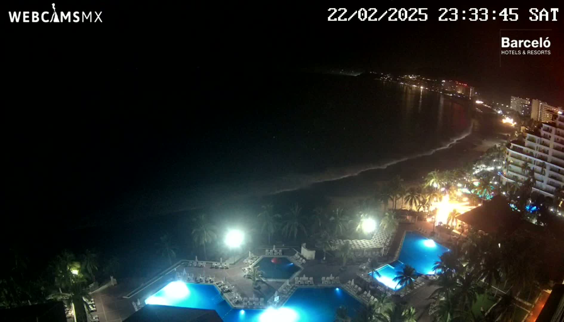 An illuminated resort with multiple pools overlooks a dark ocean shoreline at night.
