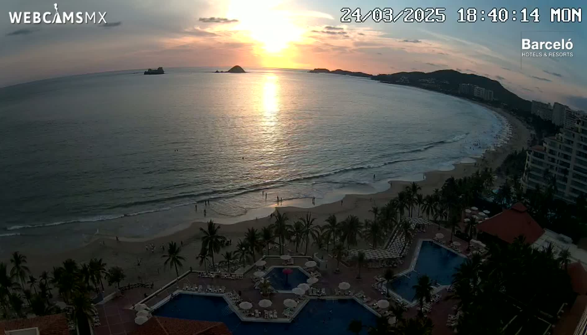 An ocean beach at sunset, with a resort featuring multiple swimming pools visible in the foreground.