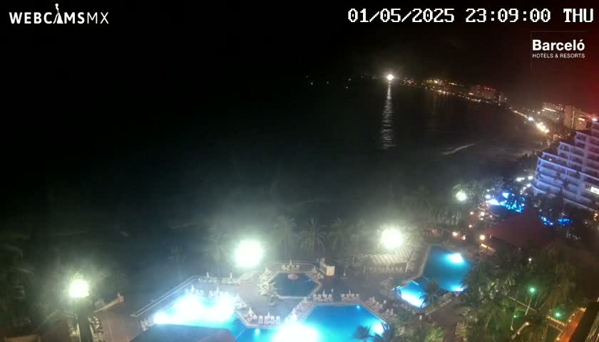 A nighttime, high-angle view of a resort complex with illuminated pools, situated near a dark ocean under a clear sky.