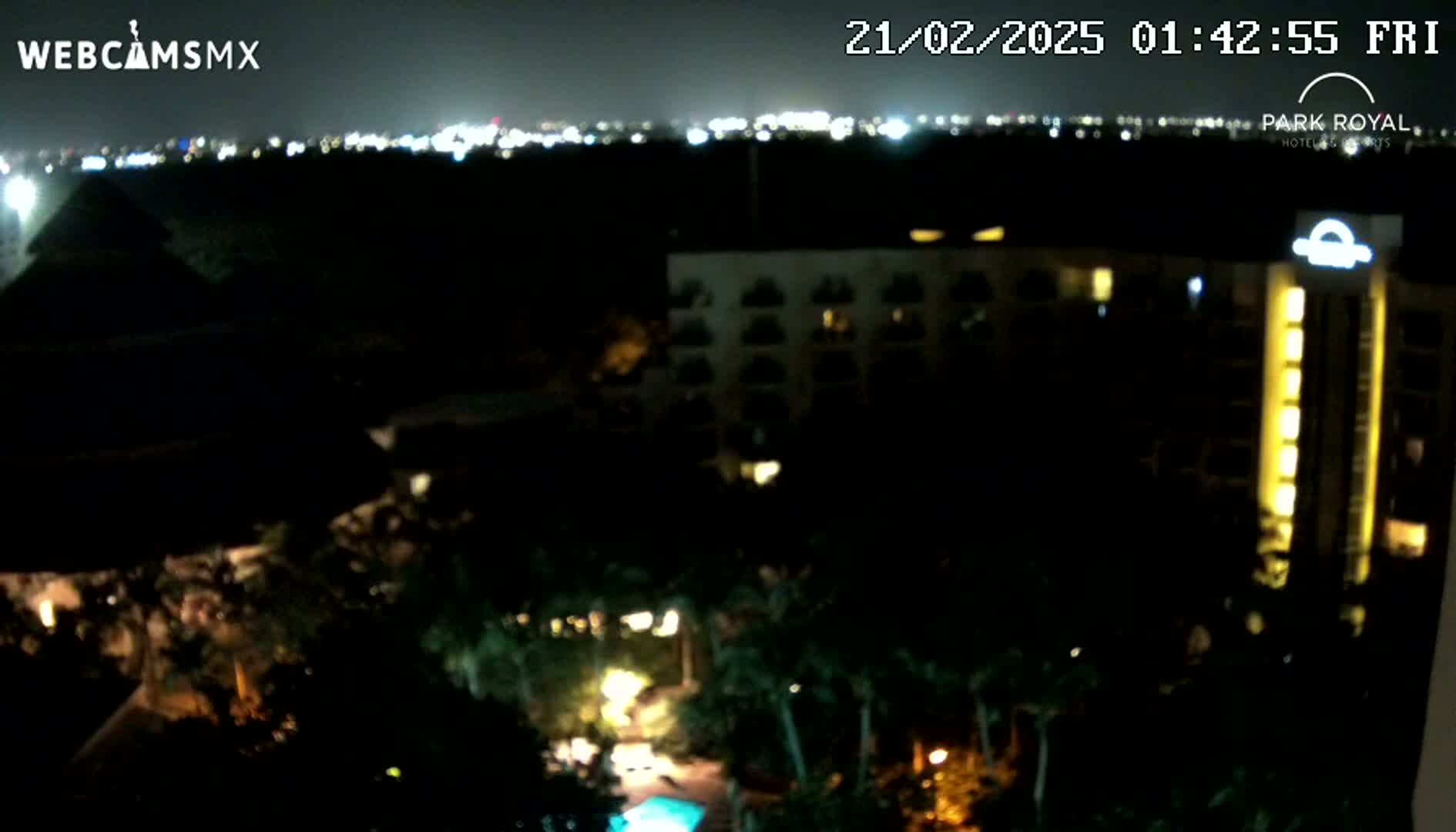 A nighttime view of a resort complex with illuminated buildings and landscaping, overlooking a city skyline in the distance under a clear sky.