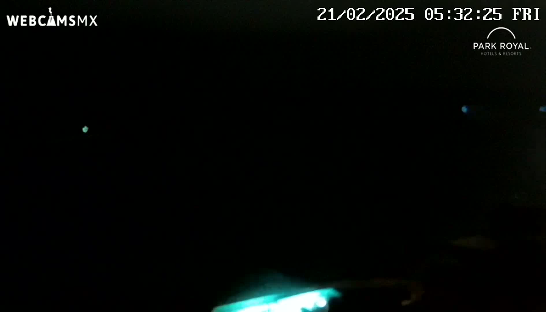 A nighttime image shows faint teal lights in the distance and a blurry teal light in the bottom right corner, under a dark sky.