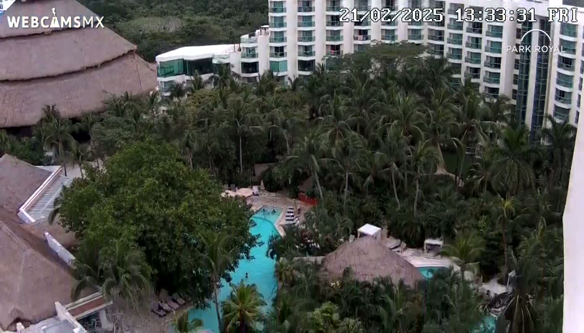 An aerial view shows a resort with multiple buildings, swimming pools, and lush tropical landscaping.