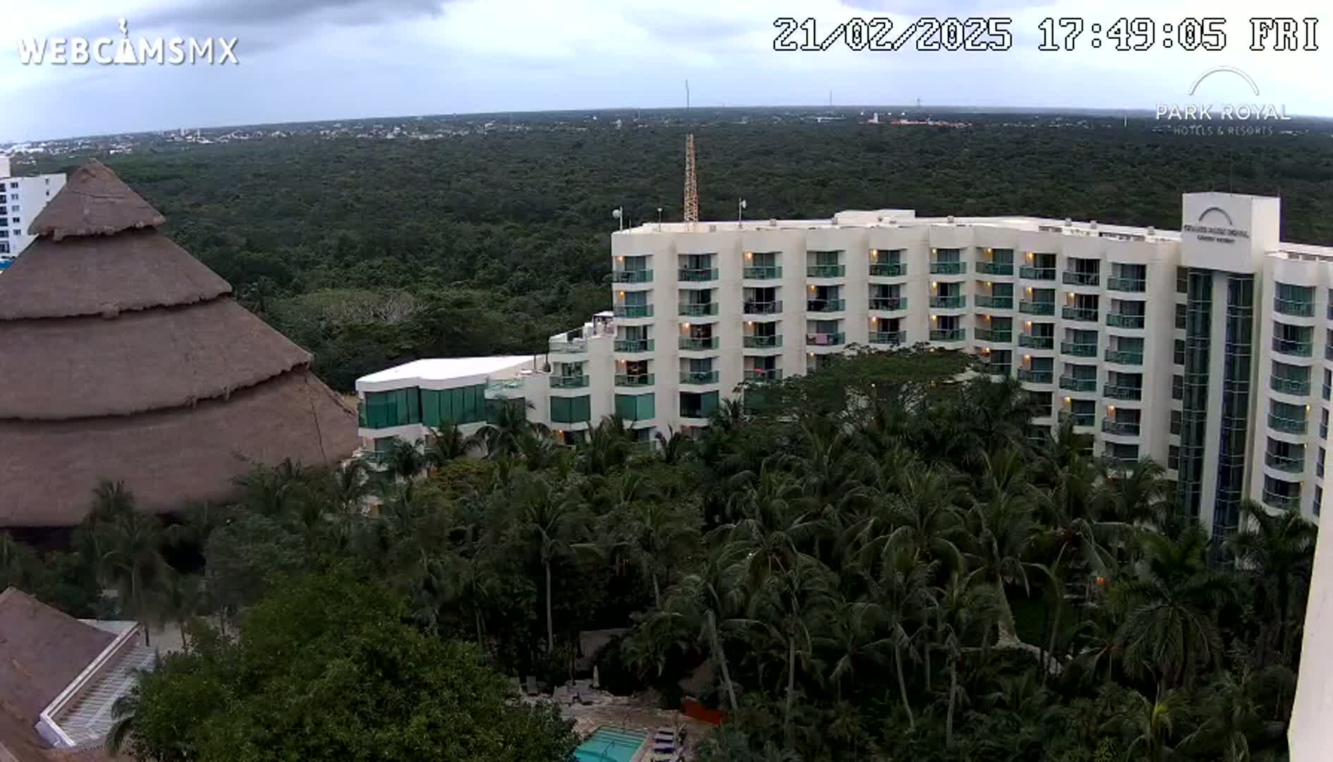 A large, multi-story hotel building sits nestled amongst lush, green tropical foliage under an overcast sky.