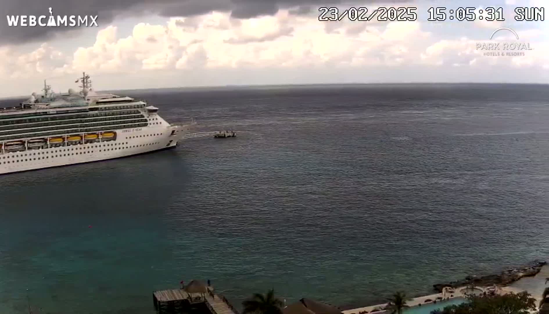 A large cruise ship is docked in calm ocean water under a partly cloudy sky.