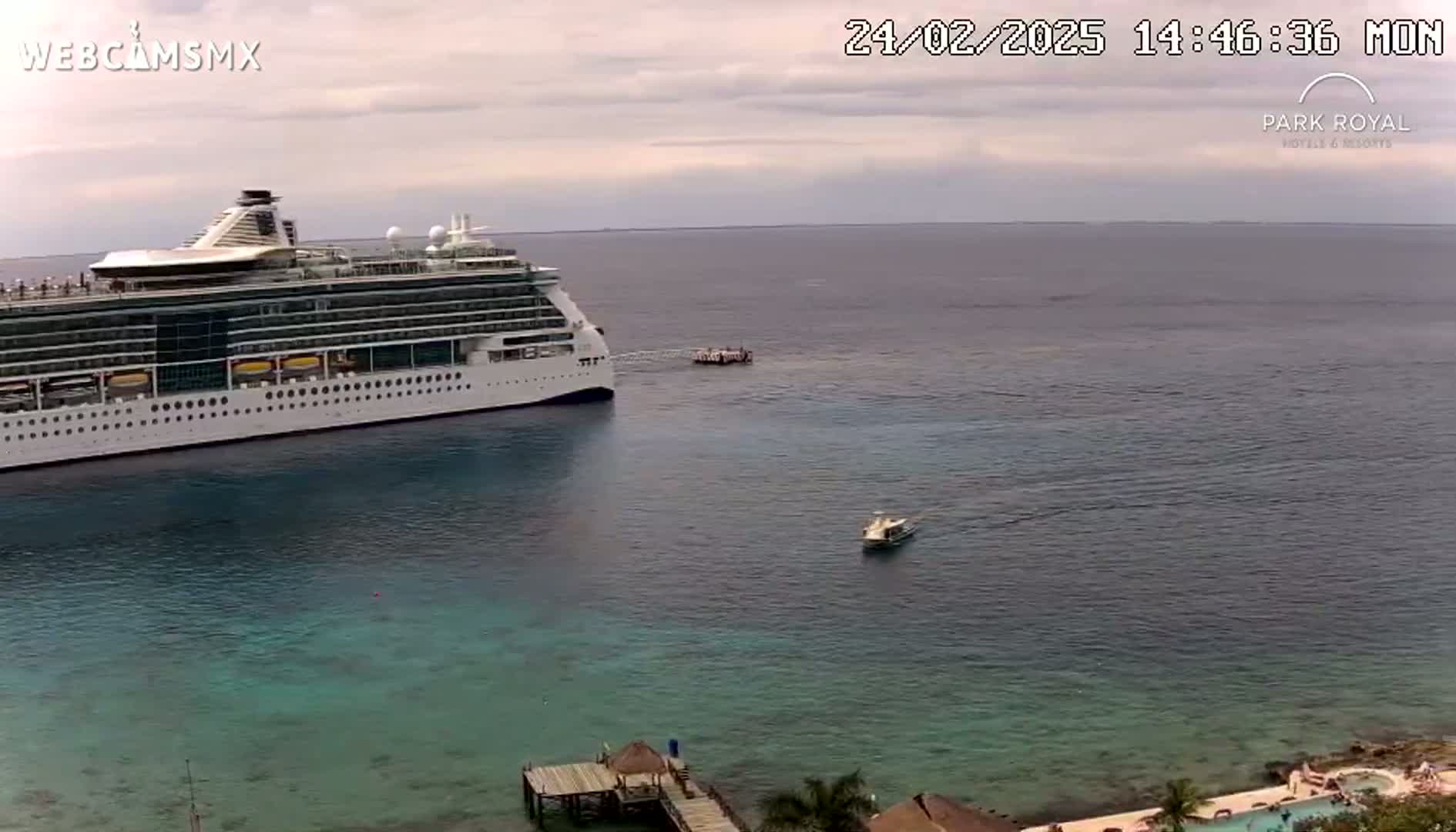 A large cruise ship is anchored in calm, clear water near a smaller boat and a pier.