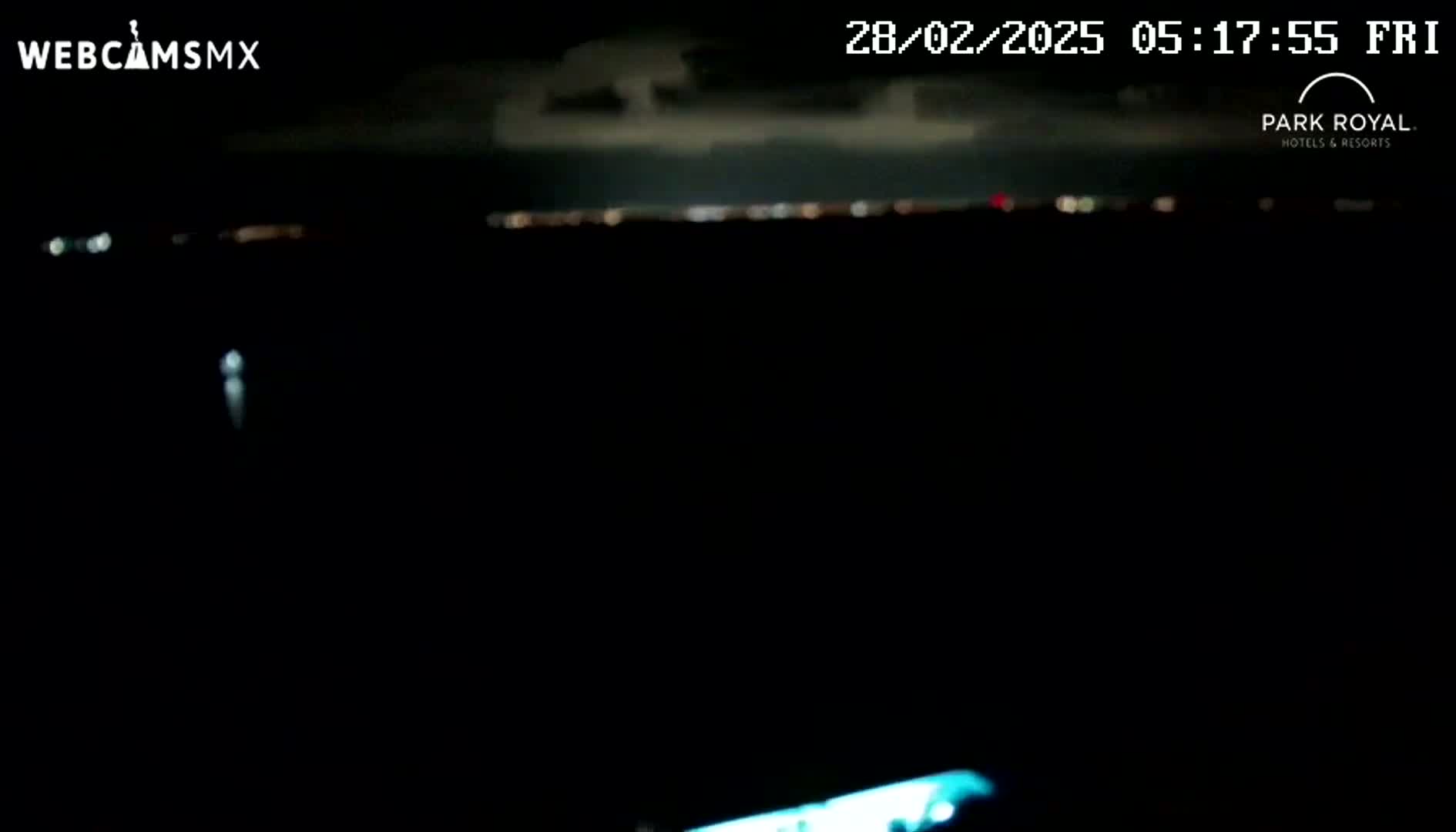 A dark nighttime scene shows a distant line of lights across the horizon, with a faint, possibly blurry light source closer in the foreground.