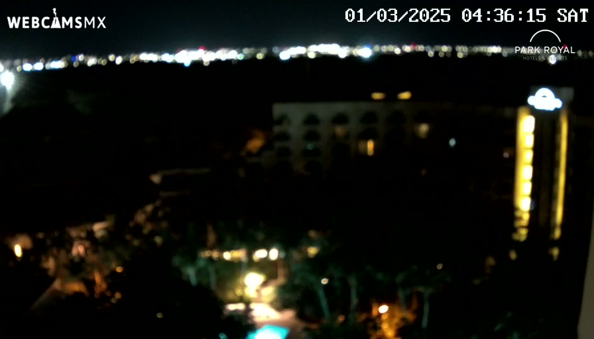 A nighttime view of a resort area with illuminated buildings and a city skyline in the distance under a clear sky.