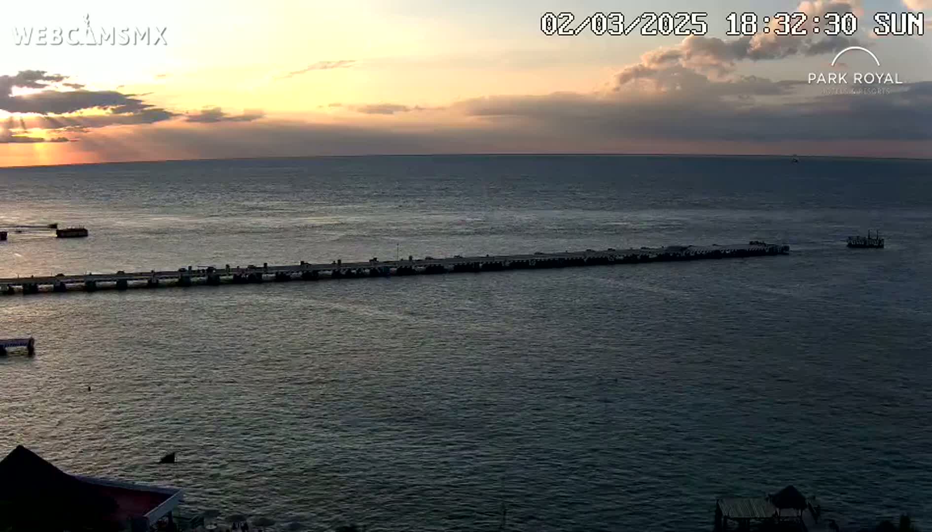 A long pier extends into a calm body of water at sunset under a partly cloudy sky.