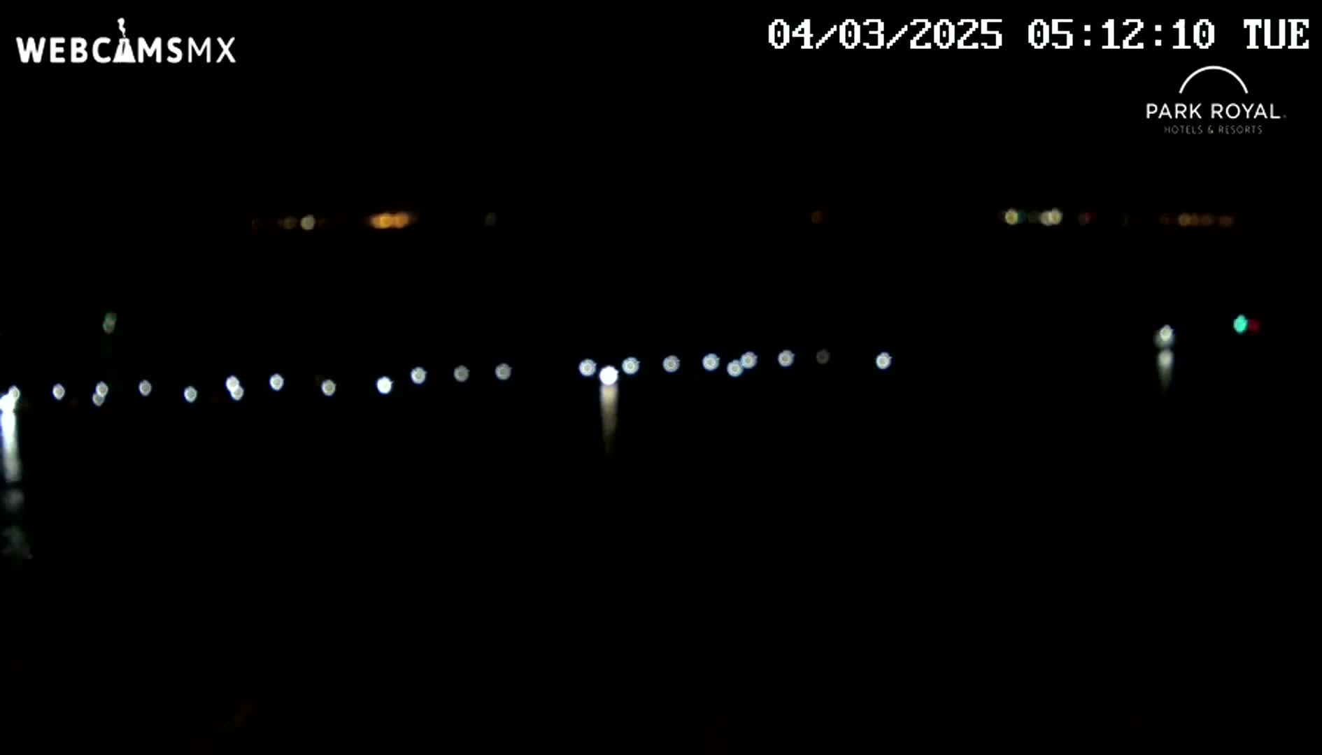 A nighttime long shot shows a line of blurred lights across a dark body of water, under a clear, dark sky.