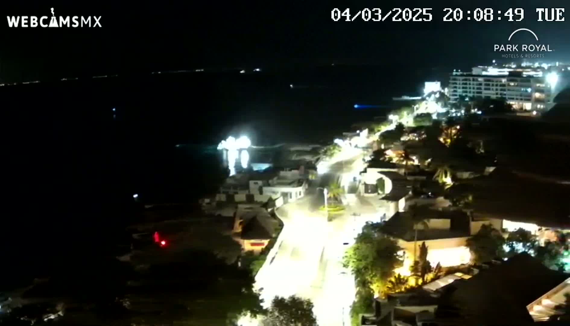A nighttime, high-angle view shows a coastal road illuminated with streetlights winding through a town next to a dark body of water.