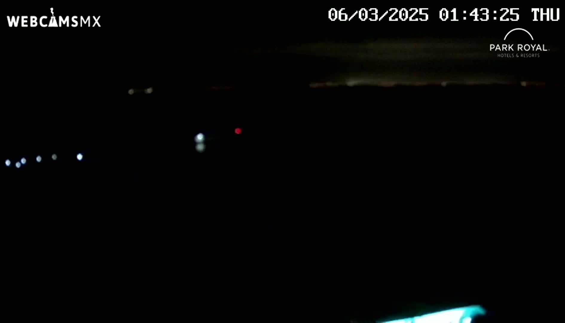 A nighttime, dark scene shows several distant, faint lights and a hint of a teal glow at the very bottom.