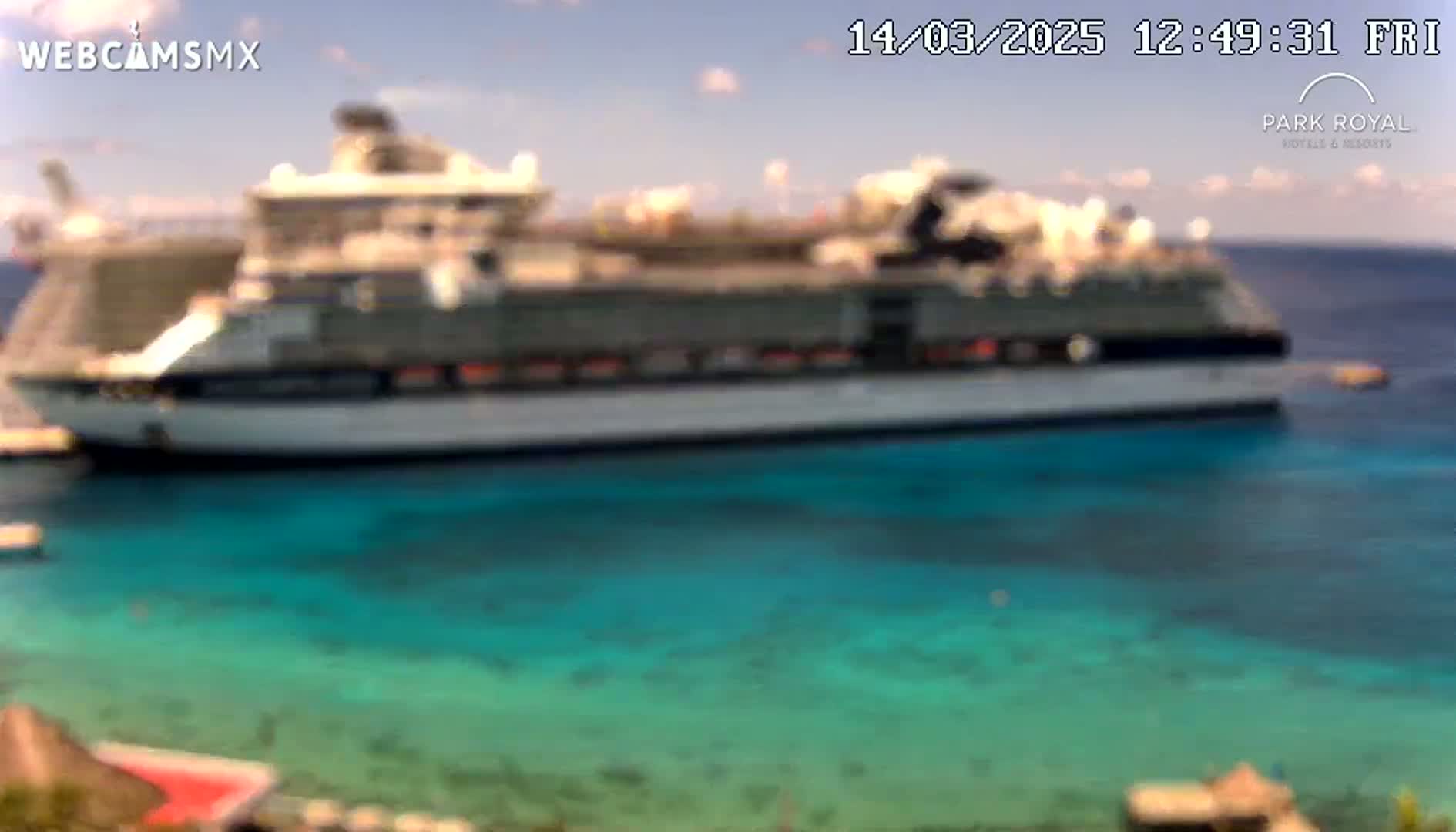 A large cruise ship is docked in clear, turquoise water under a mostly sunny sky.