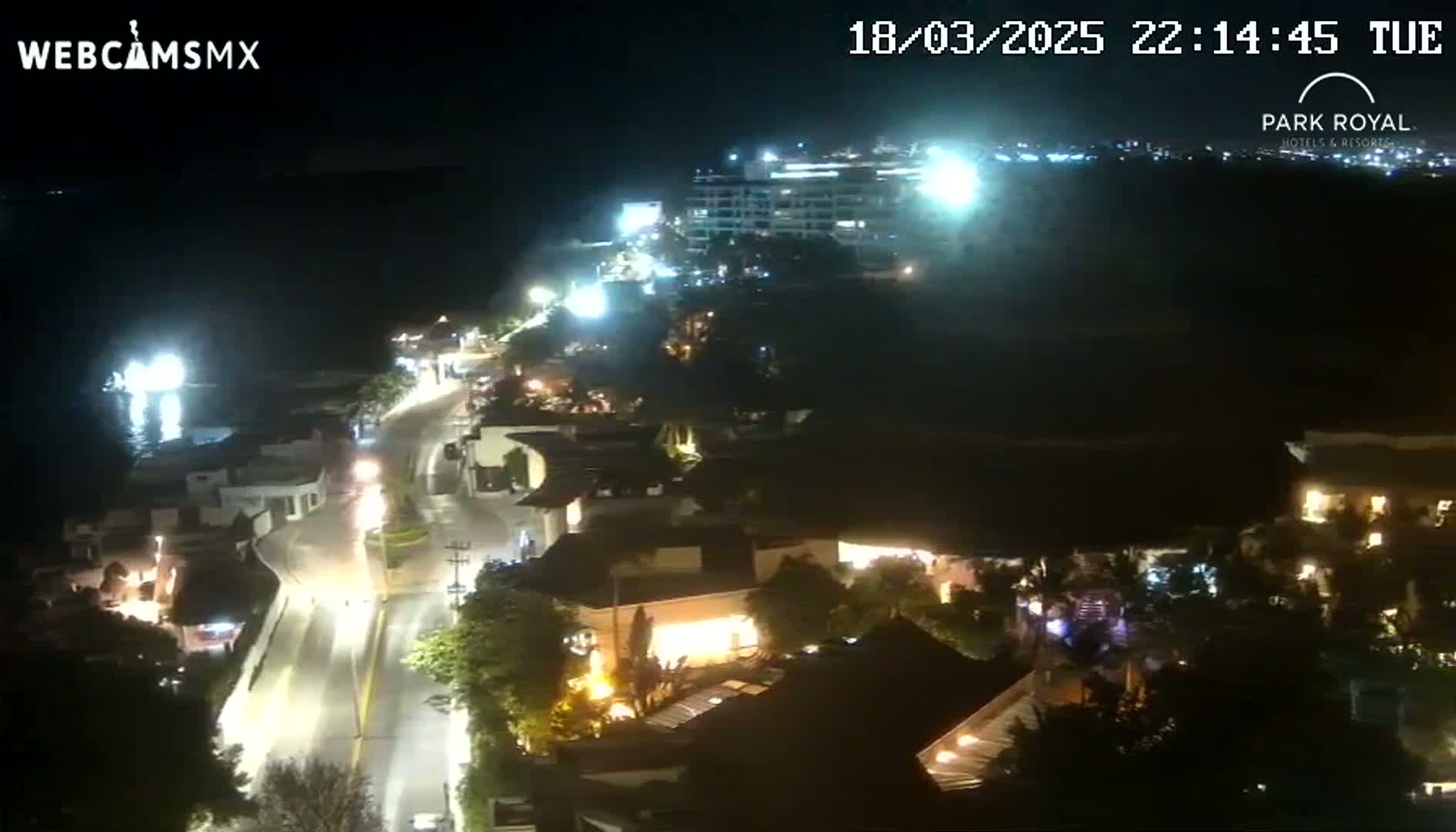 A nighttime, high-angle view shows a coastal town with brightly lit buildings and streets along a dark body of water.
