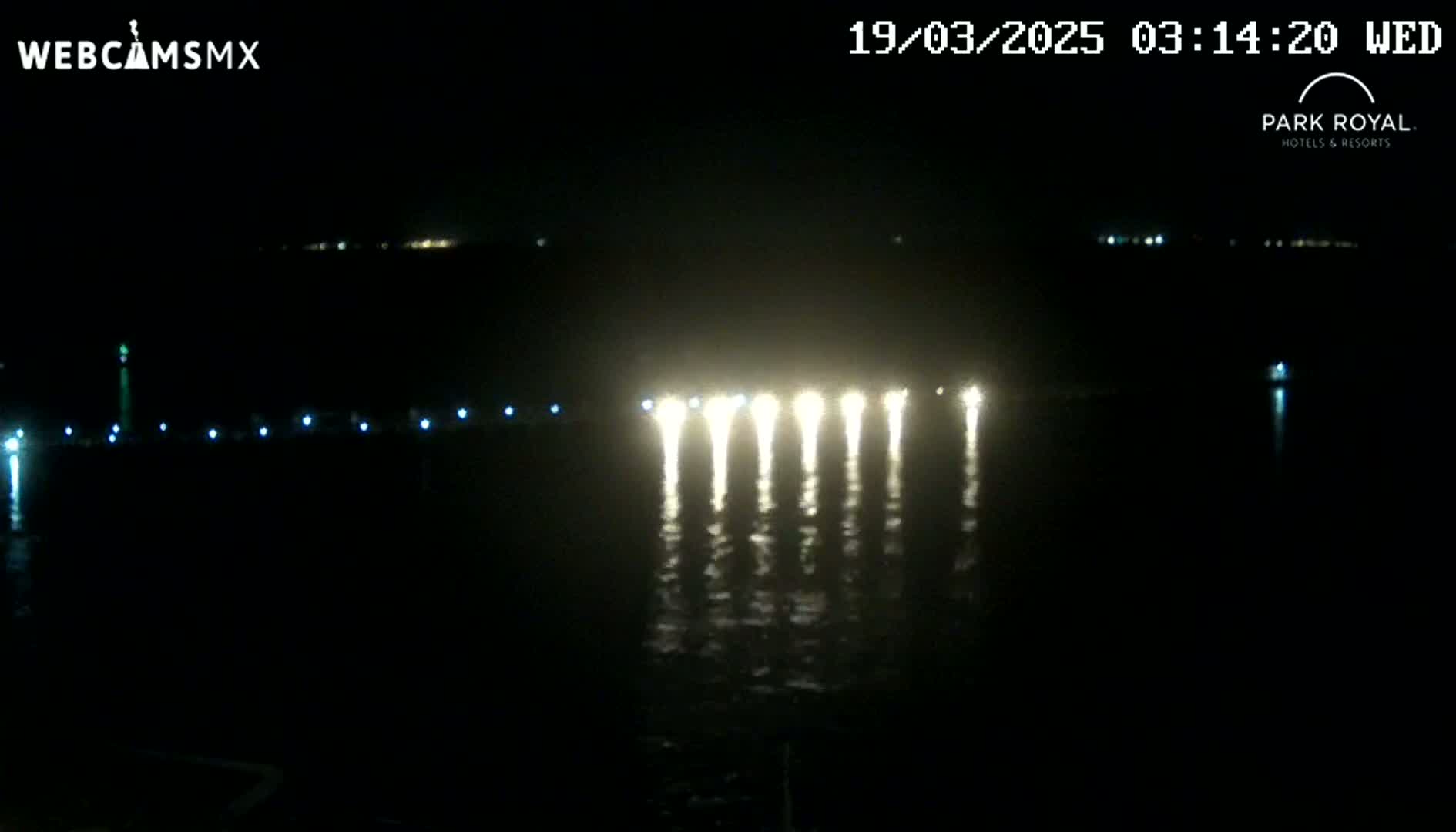 A nighttime view of a body of water with bright lights reflecting on its surface, and faint lights visible in the distance.