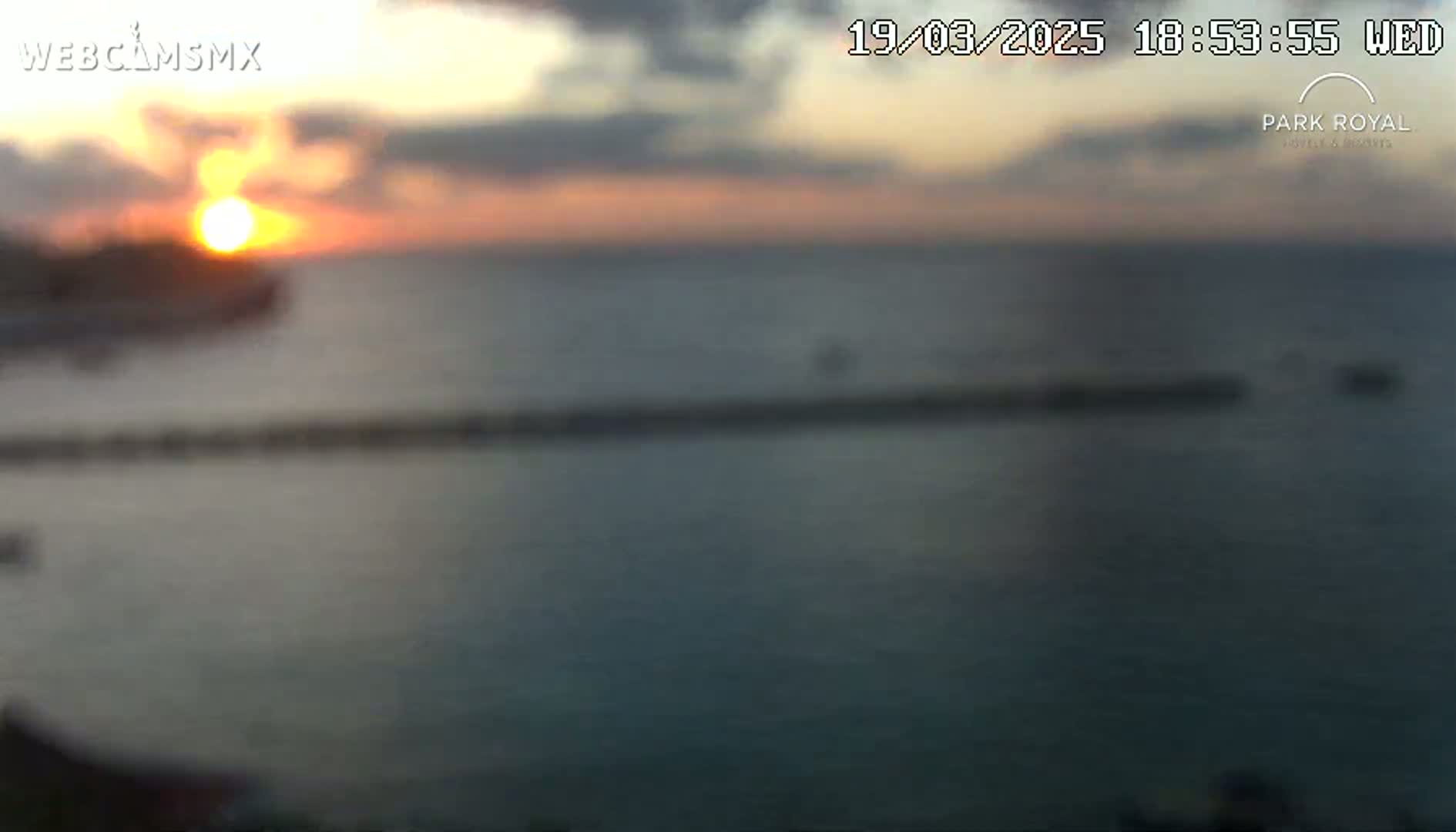 A blurry sunset over a calm ocean with a long, low structure in the water.