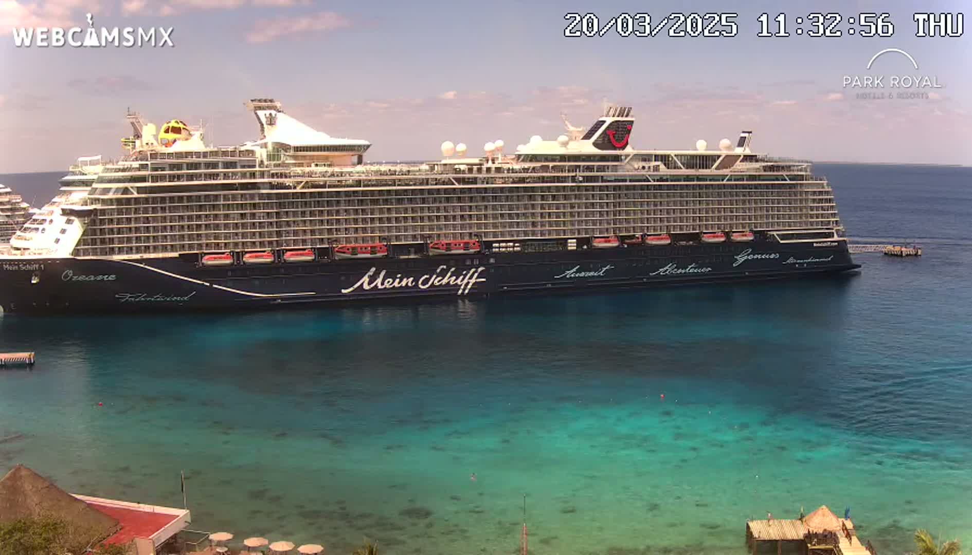 A large cruise ship is docked in clear, turquoise water under a mostly sunny sky.