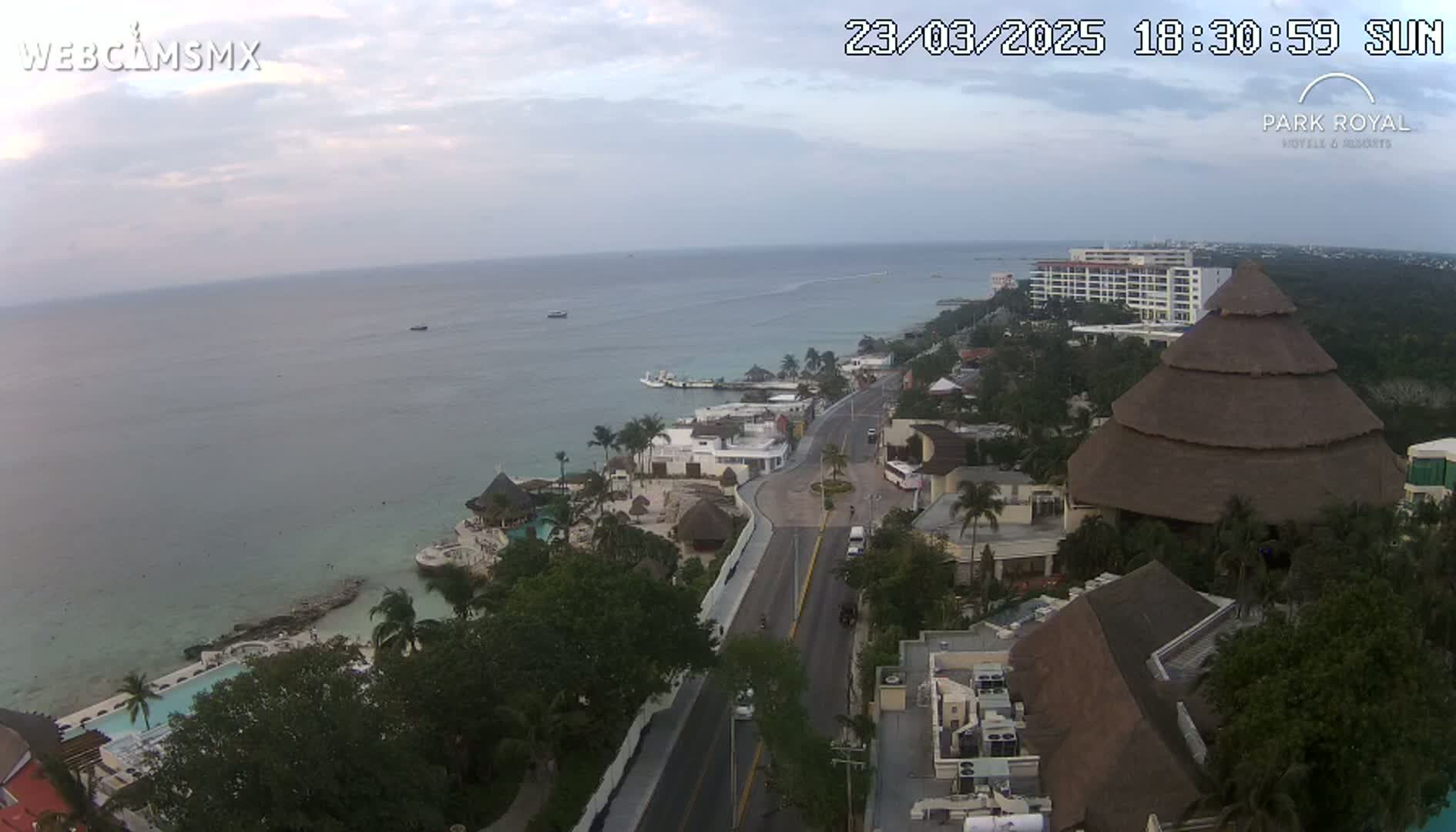 An aerial view shows a coastal town with resorts, a road, and calm ocean under an overcast sky.