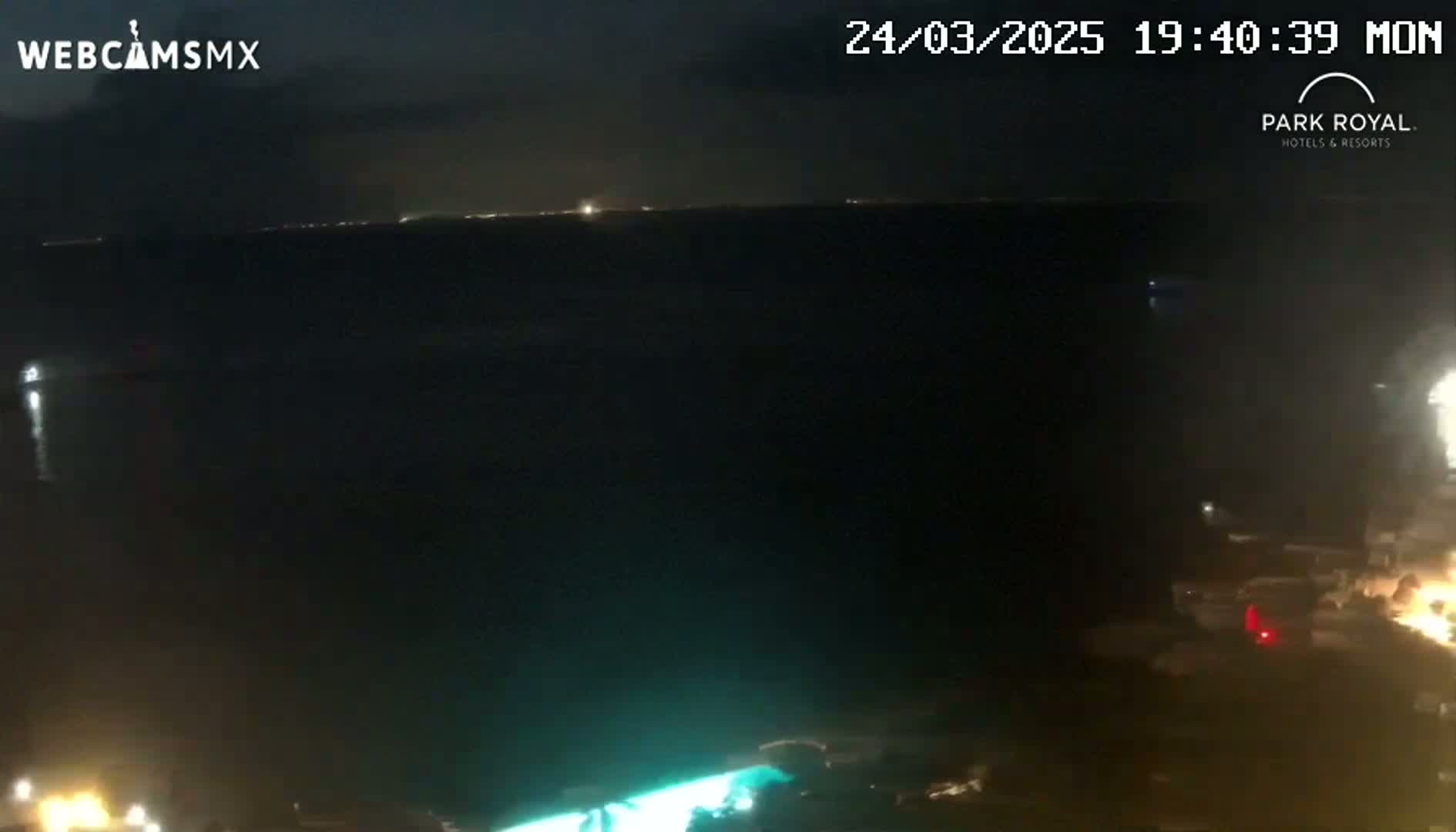 A nighttime view of a dark body of water with faint lights visible on the horizon and some lights near the bottom of the frame.