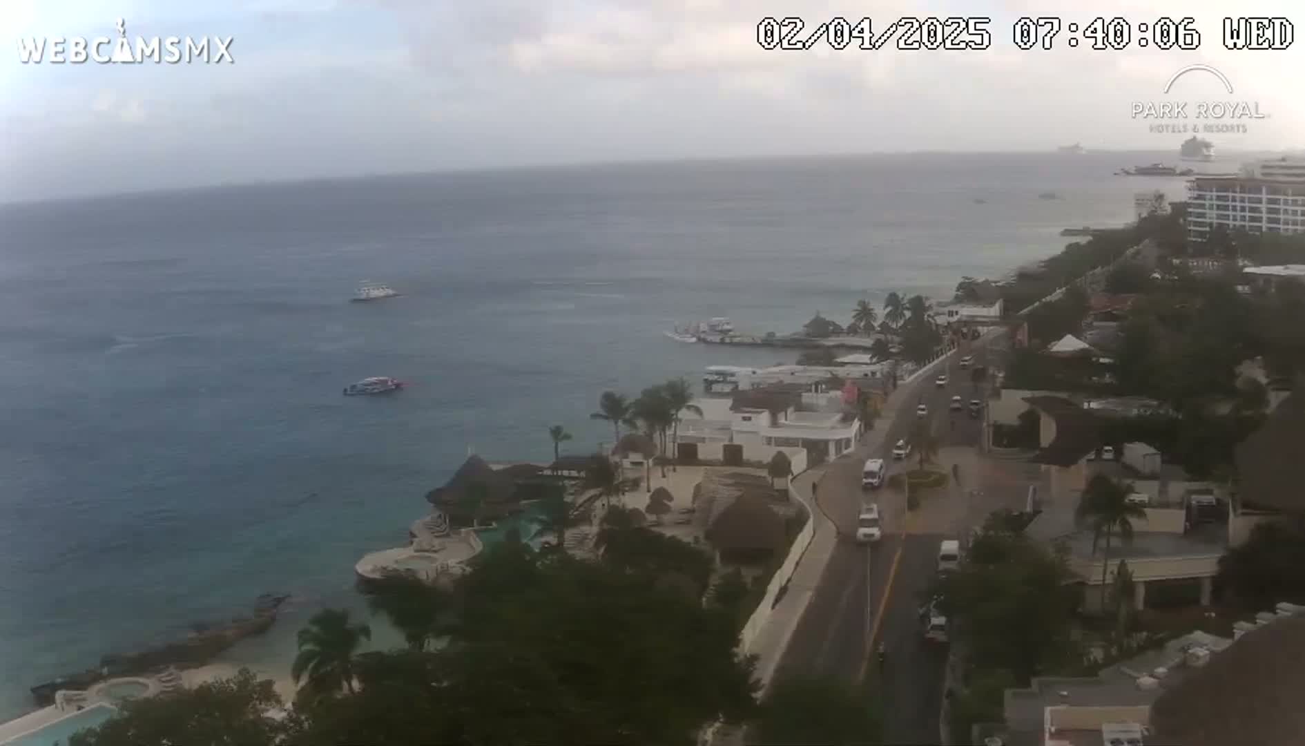An overcast coastal scene shows a resort town with a road leading down to the ocean, where several boats are visible on calm water.
