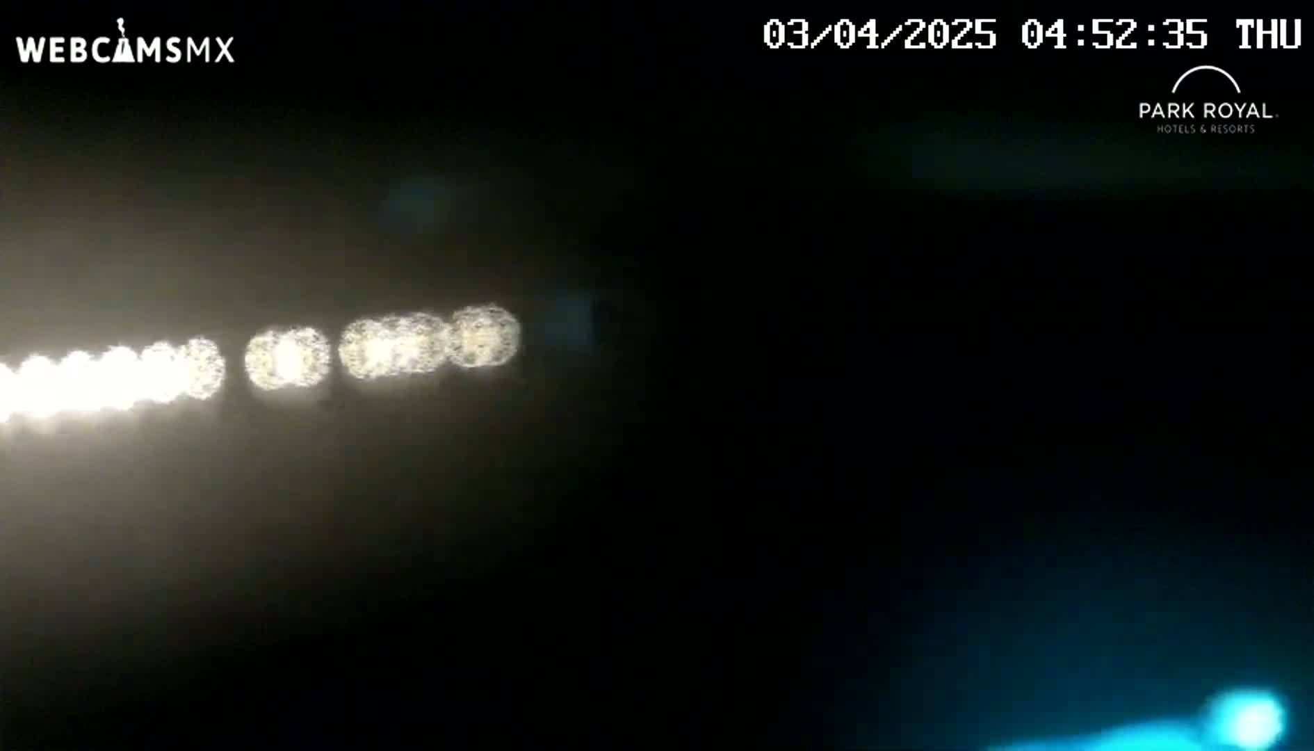 A blurry image shows a hazy, dark night scene with a line of bright lights in the distance and a faint bluish glow near the bottom.