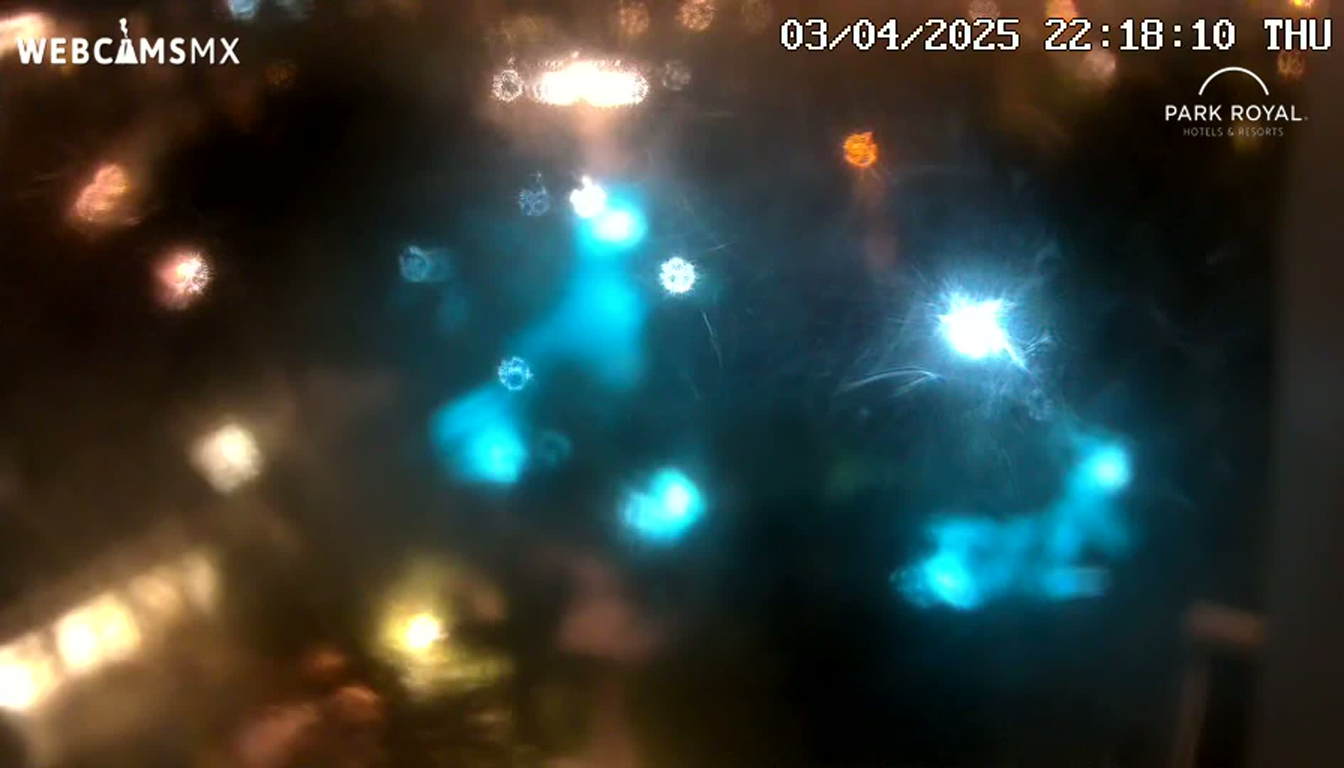 Blurred nighttime lights appear as glowing orbs of various colors through a rain-streaked surface.