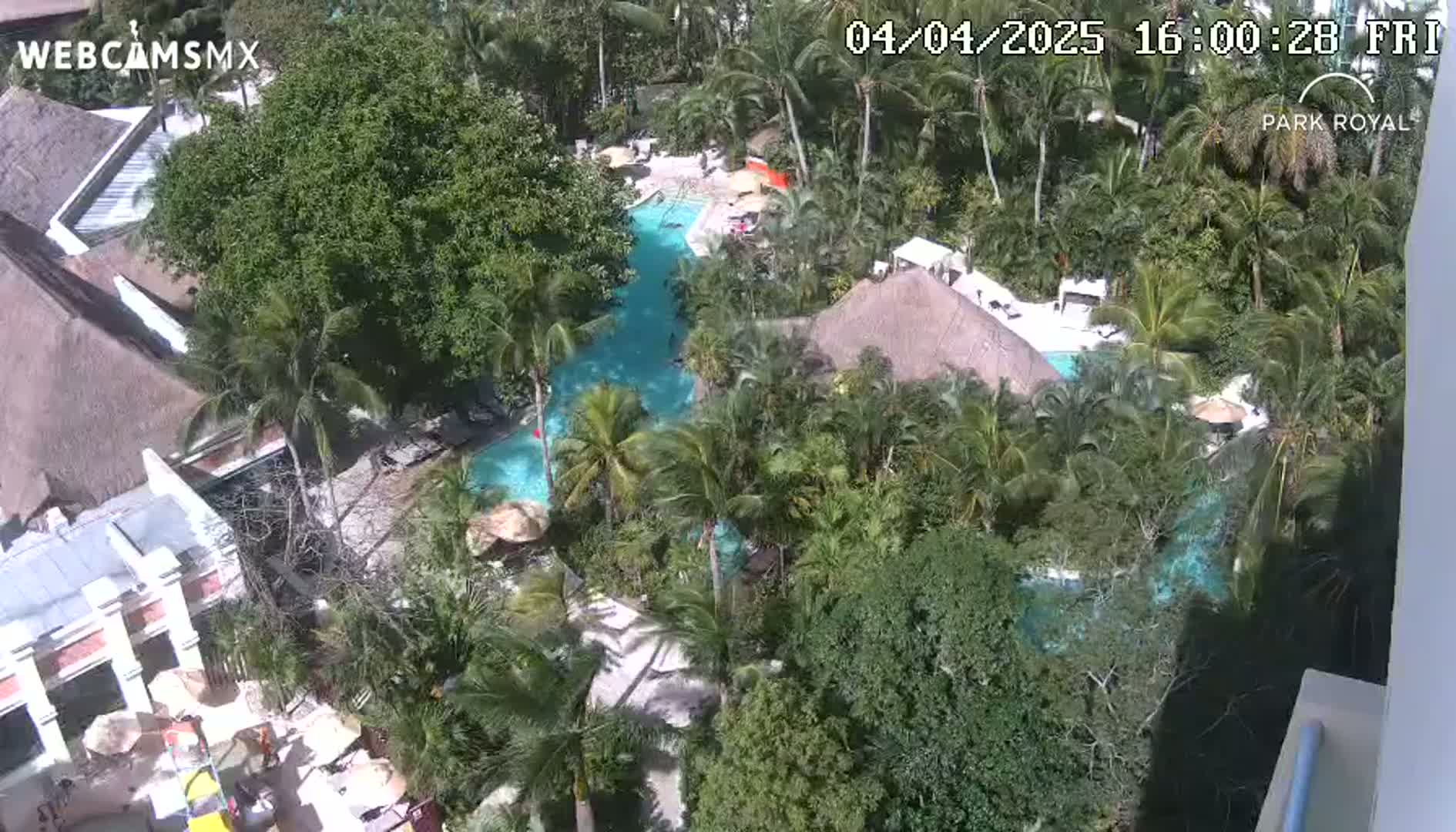 An aerial view shows a resort with multiple pools winding through lush tropical landscaping on a sunny day.