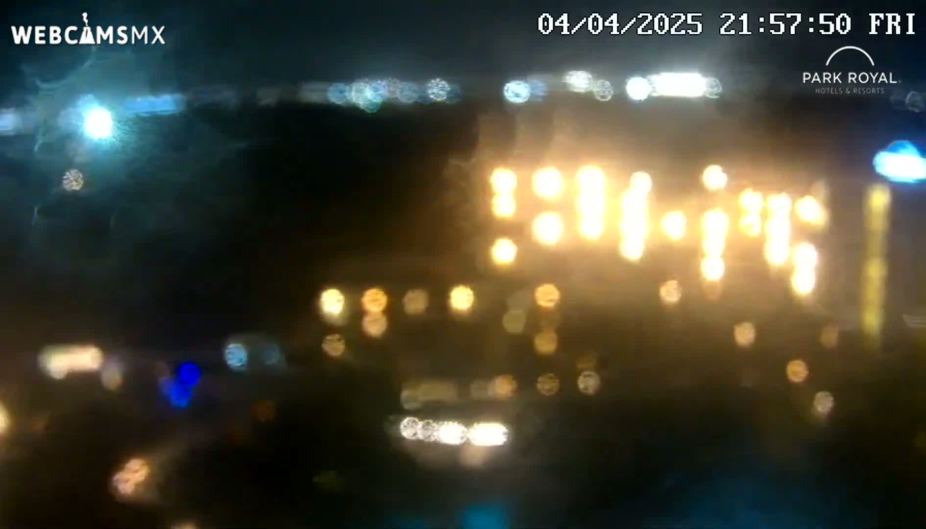 A blurry nighttime view of brightly lit buildings and vehicles through rain-streaked glass.