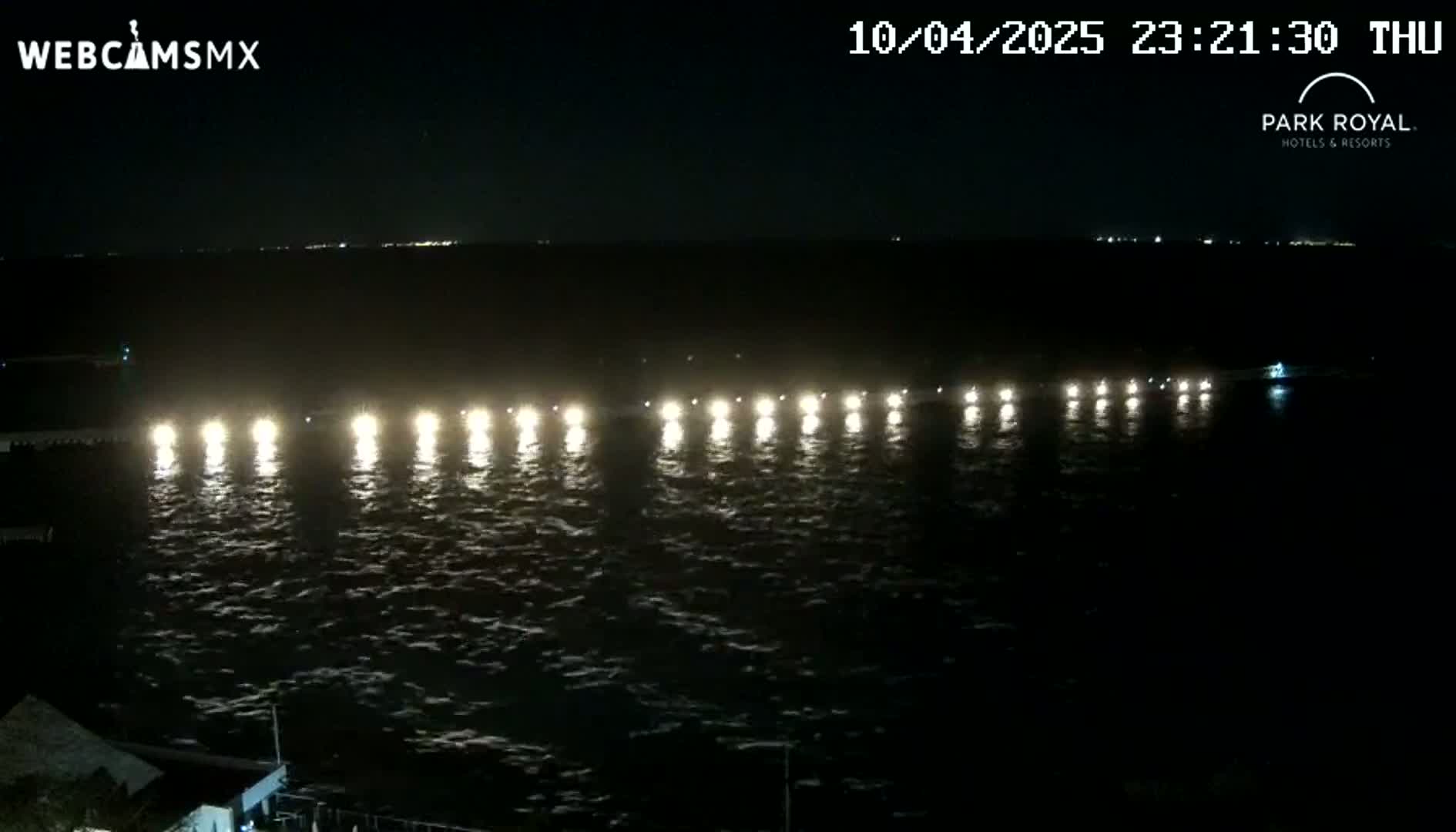 A nighttime view of a body of water shows a line of lights extending across it, reflecting on the slightly choppy surface.