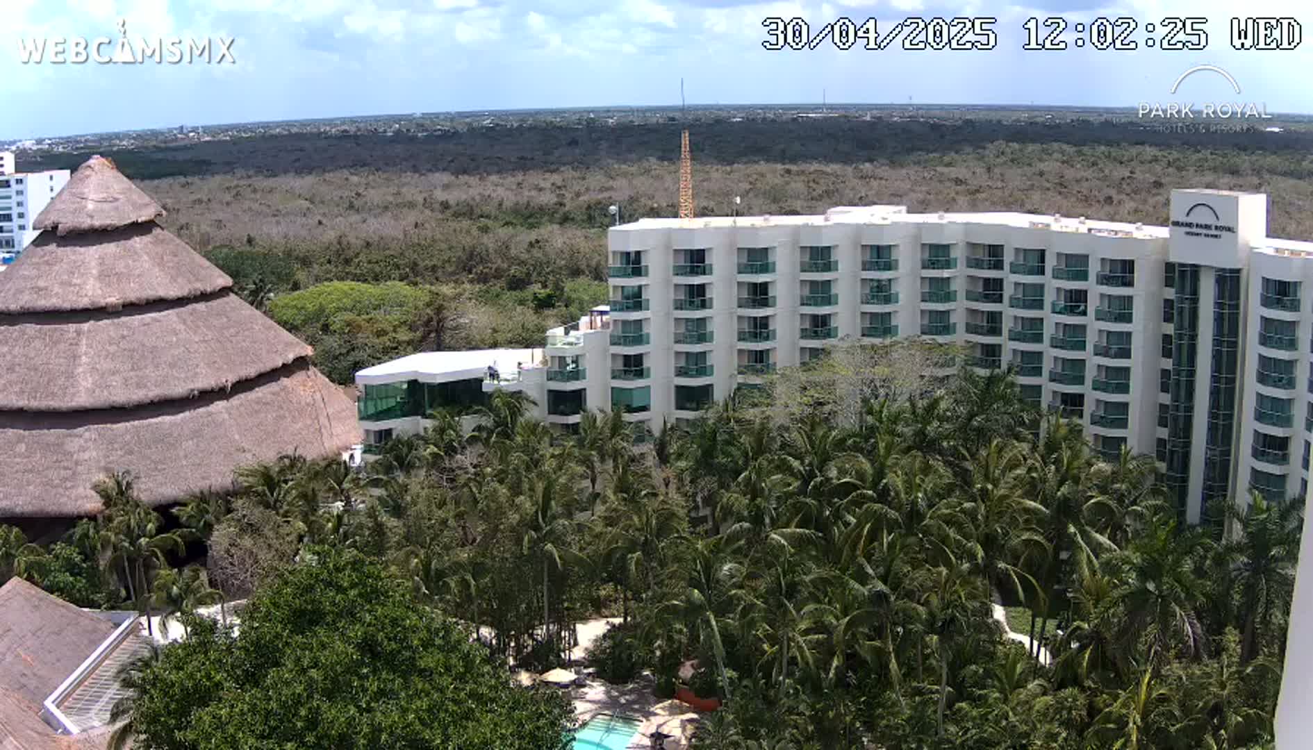 A large, multi-story hotel is nestled among lush tropical vegetation under a partly cloudy sky.