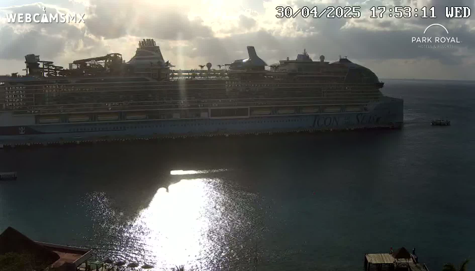 A large cruise ship is docked in calm water under a partly cloudy sunset.