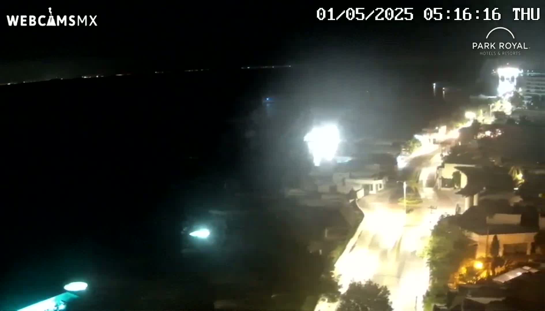 A nighttime, high-angle view shows a coastal town with brightly lit streets and buildings next to a dark body of water.