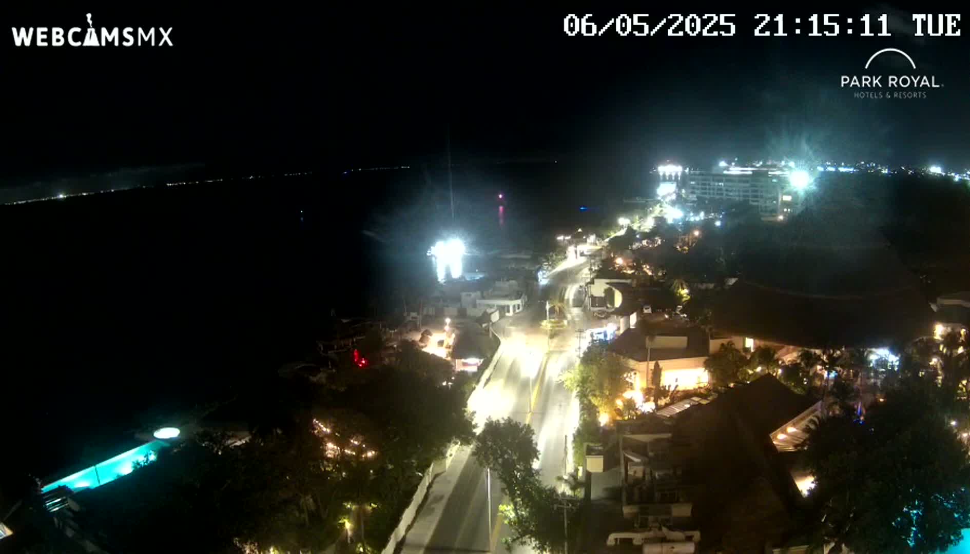 A nighttime, high-angle view of a coastal town with brightly lit buildings and a road leading to a dark body of water.
