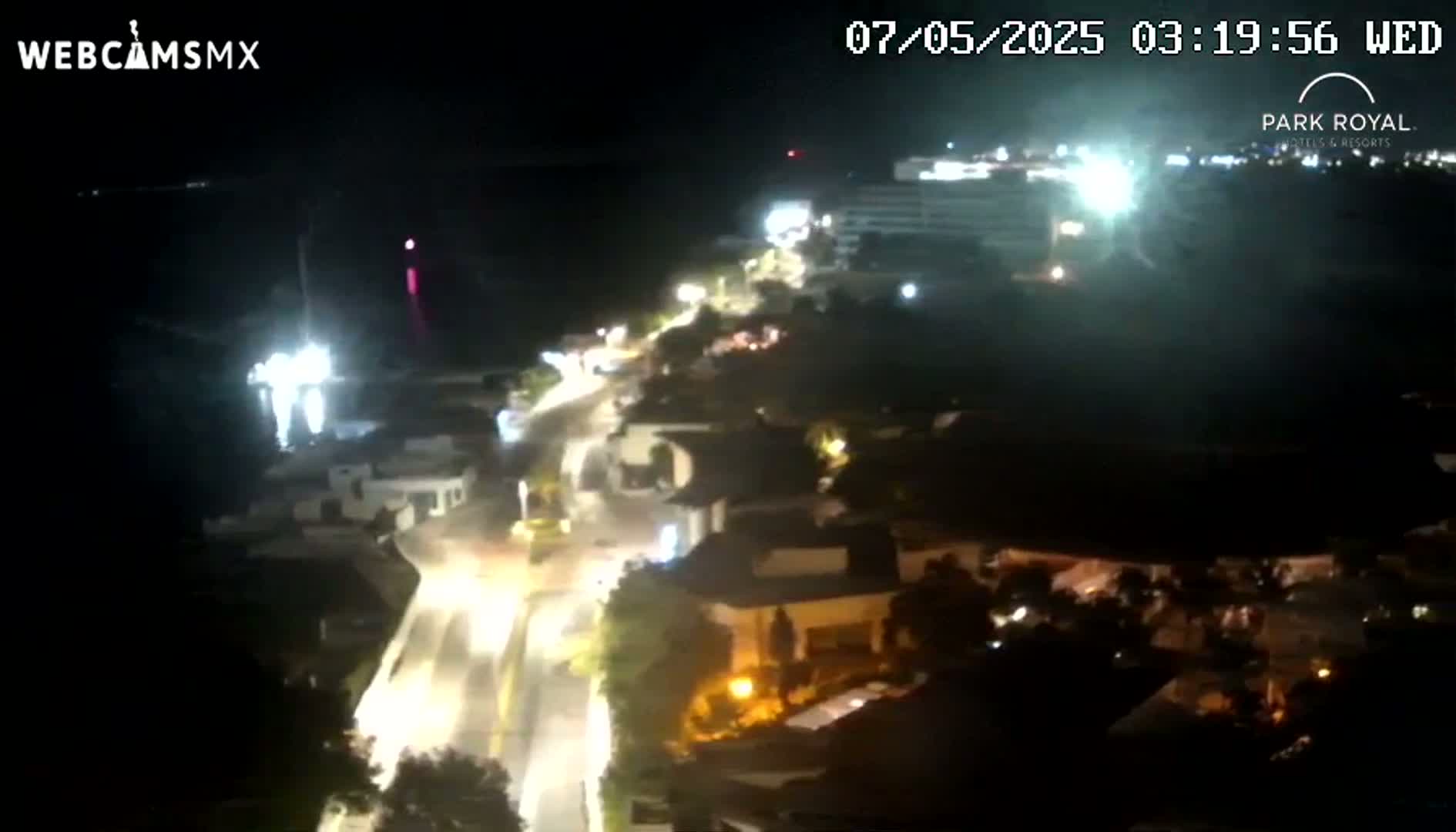 A nighttime, high-angle view shows a coastal town with illuminated streets and buildings near a dark body of water.