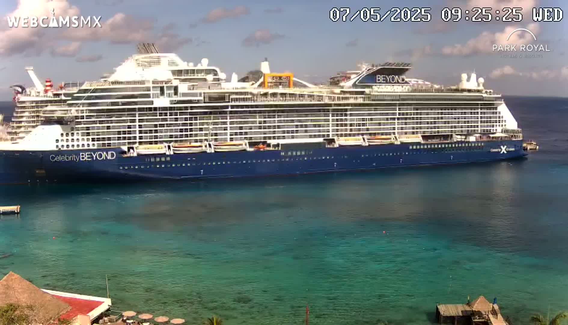 A large cruise ship is docked in clear, turquoise water under a mostly sunny sky.