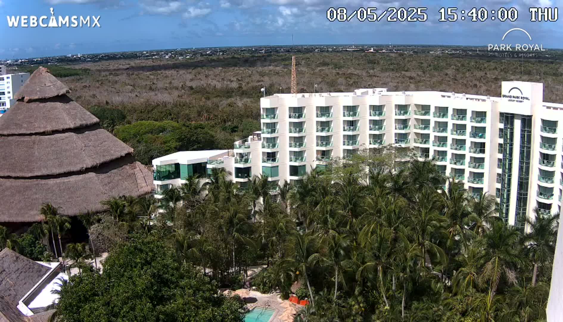 A large hotel complex is nestled within a lush, tropical landscape under a partly cloudy sky.