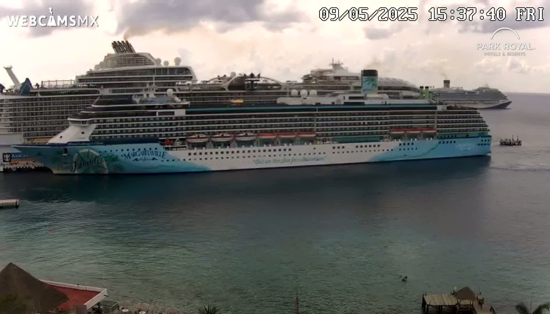 Three large cruise ships are docked in calm, somewhat cloudy water.