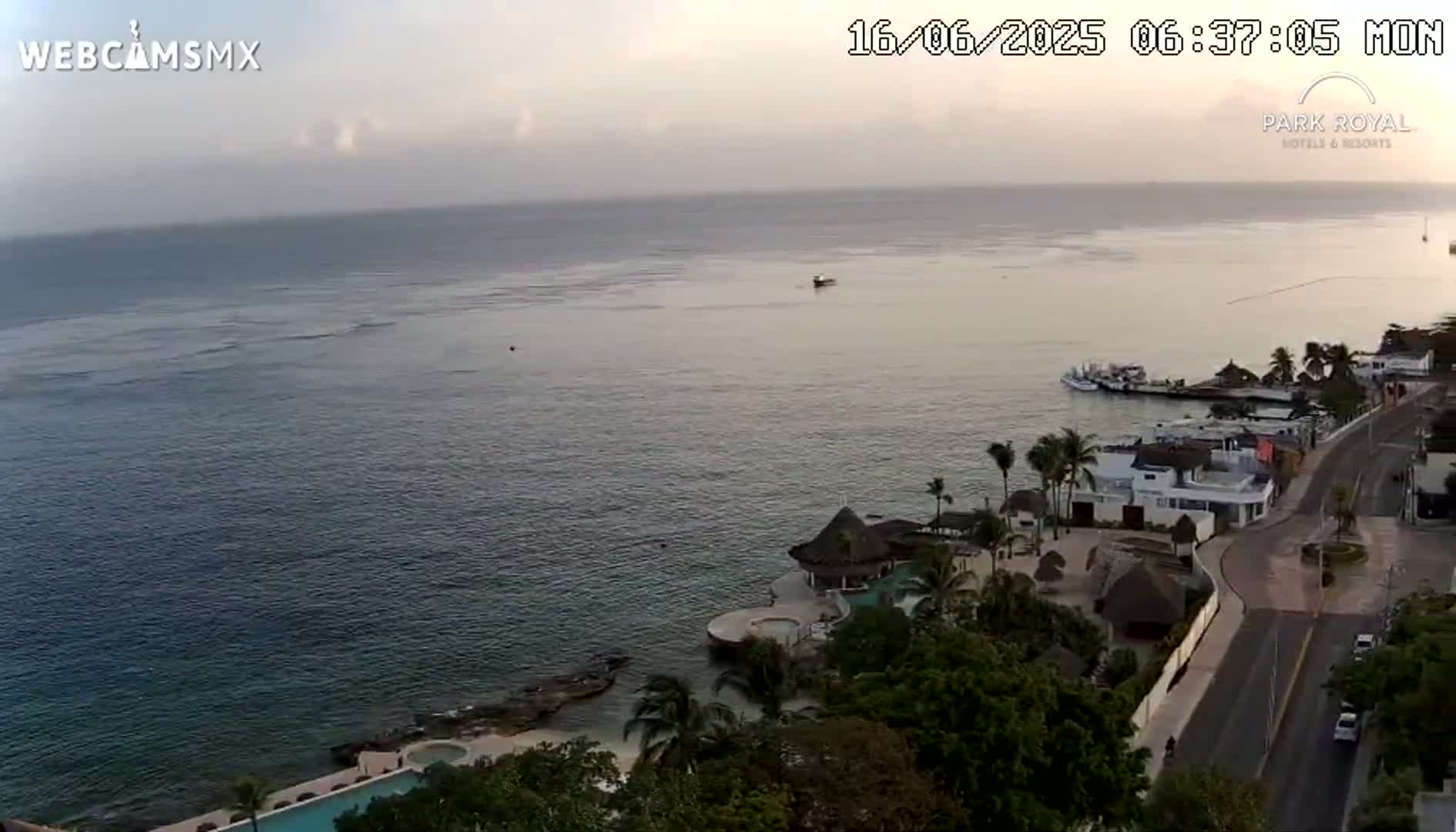 An aerial view shows a calm ocean under an overcast sky, with a coastal resort and road visible in the foreground.