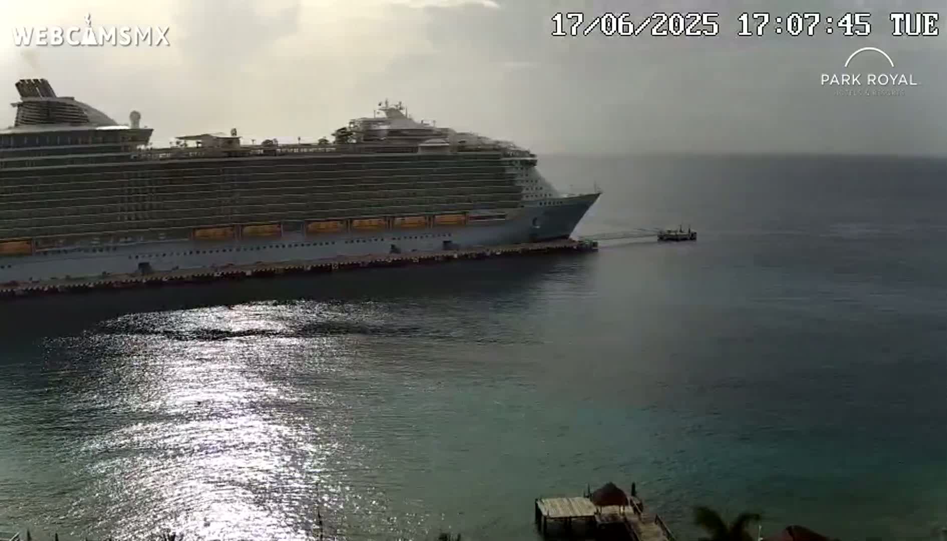 A large cruise ship is docked at a port on a partly cloudy day.