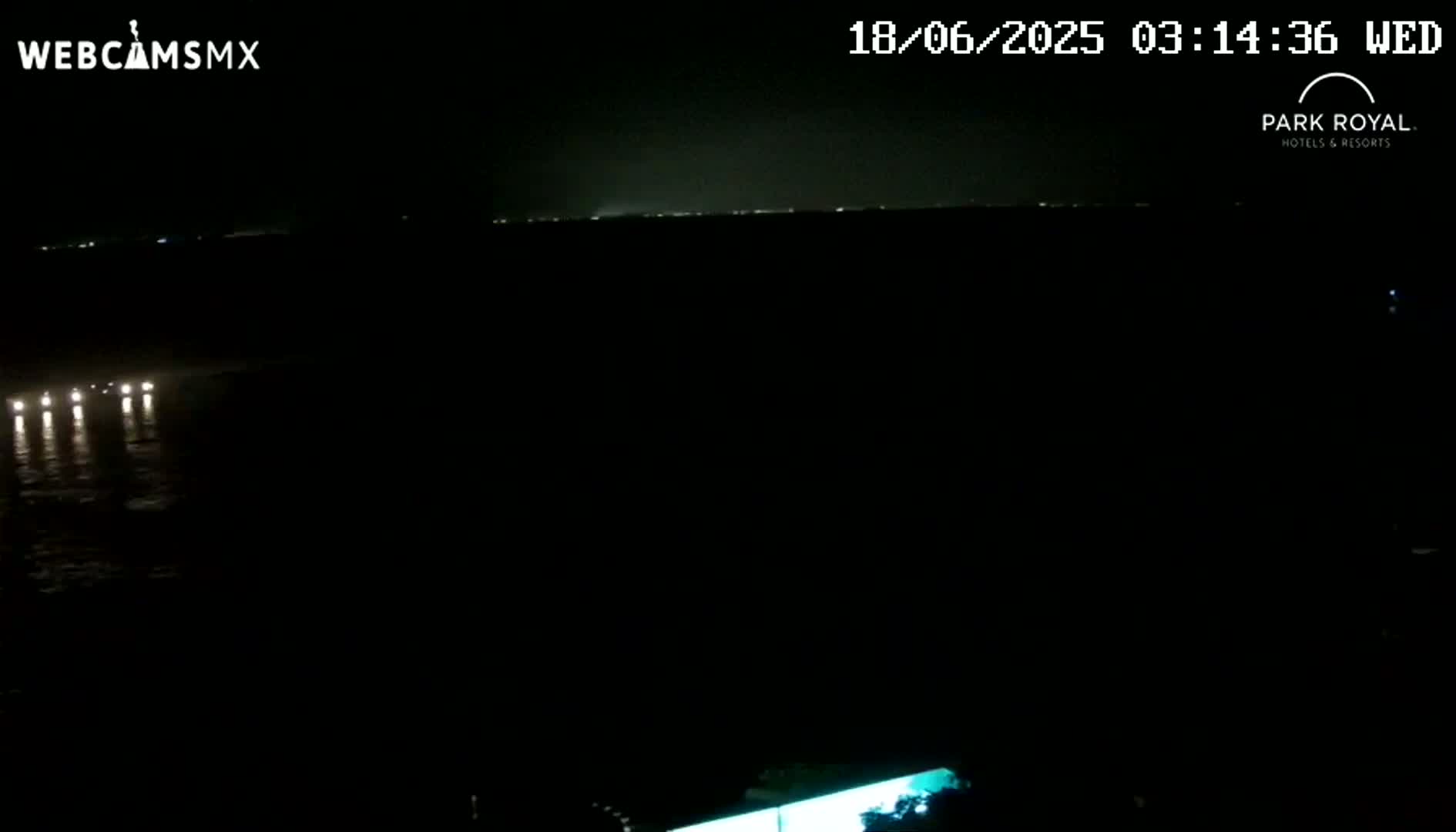 A nighttime, dark view of a body of water with a few distant lights reflecting on the surface and a faint light line on the horizon.