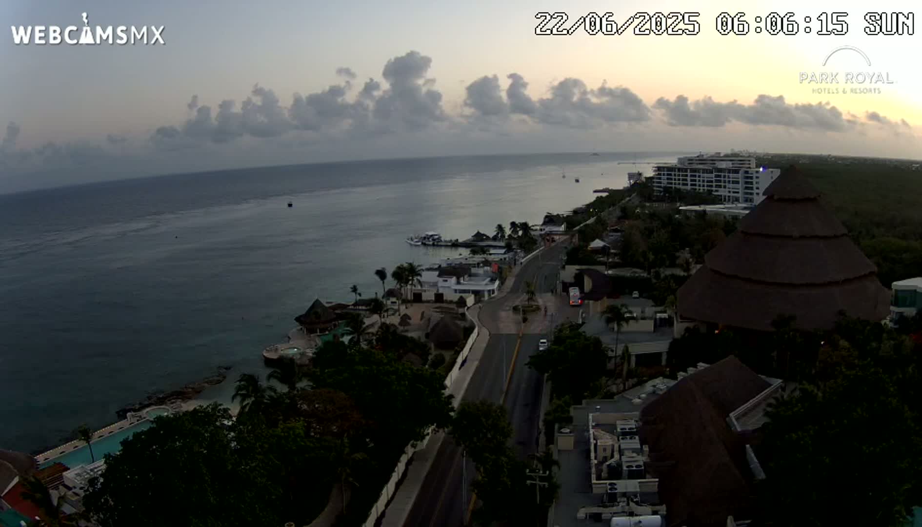 An aerial view shows a coastal resort town at dawn under a partly cloudy sky, with calm ocean waters visible in the background.
