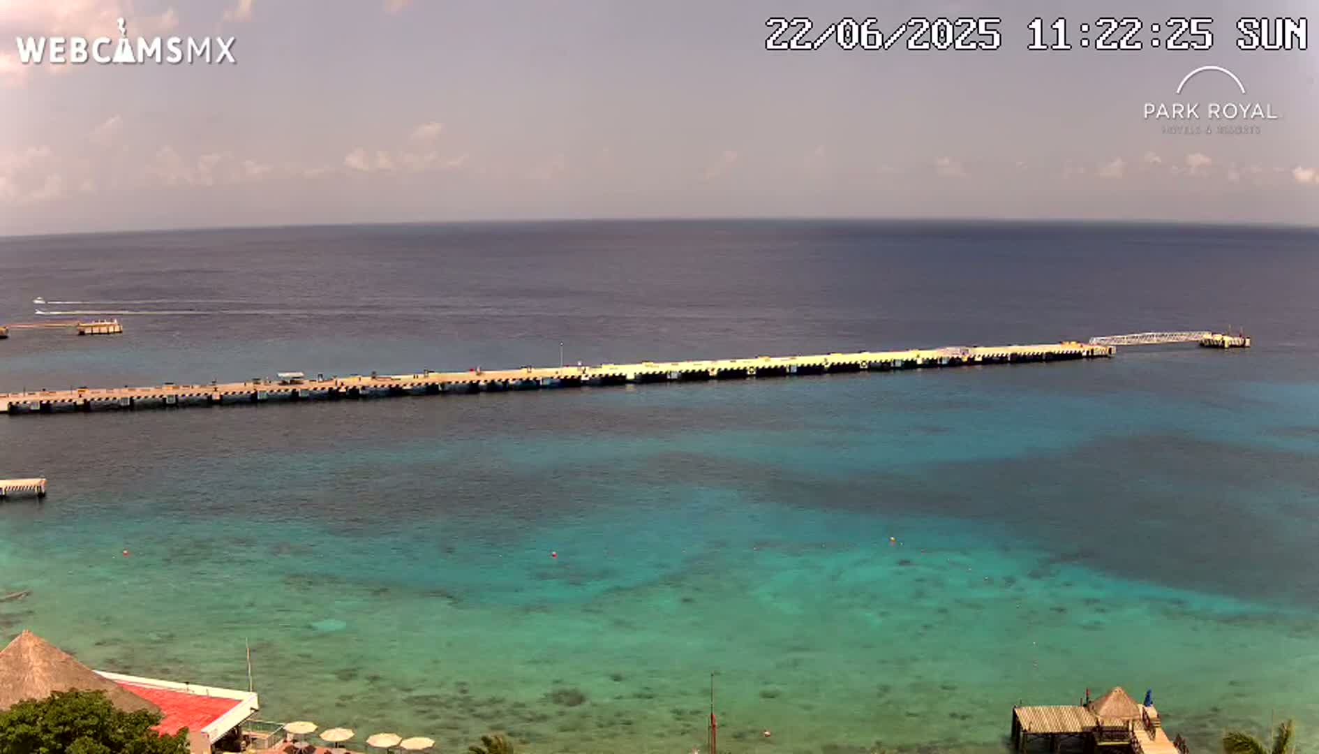 A long pier extends into a calm, clear turquoise ocean under a partly cloudy sky.