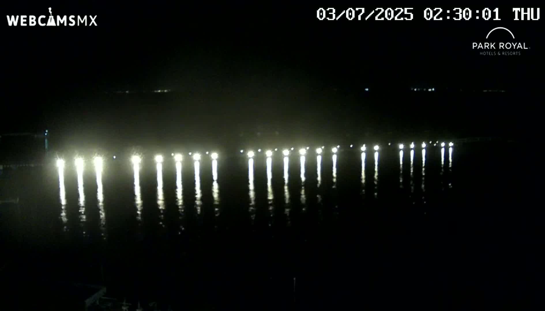 At night, a series of lights are reflected in calm water.