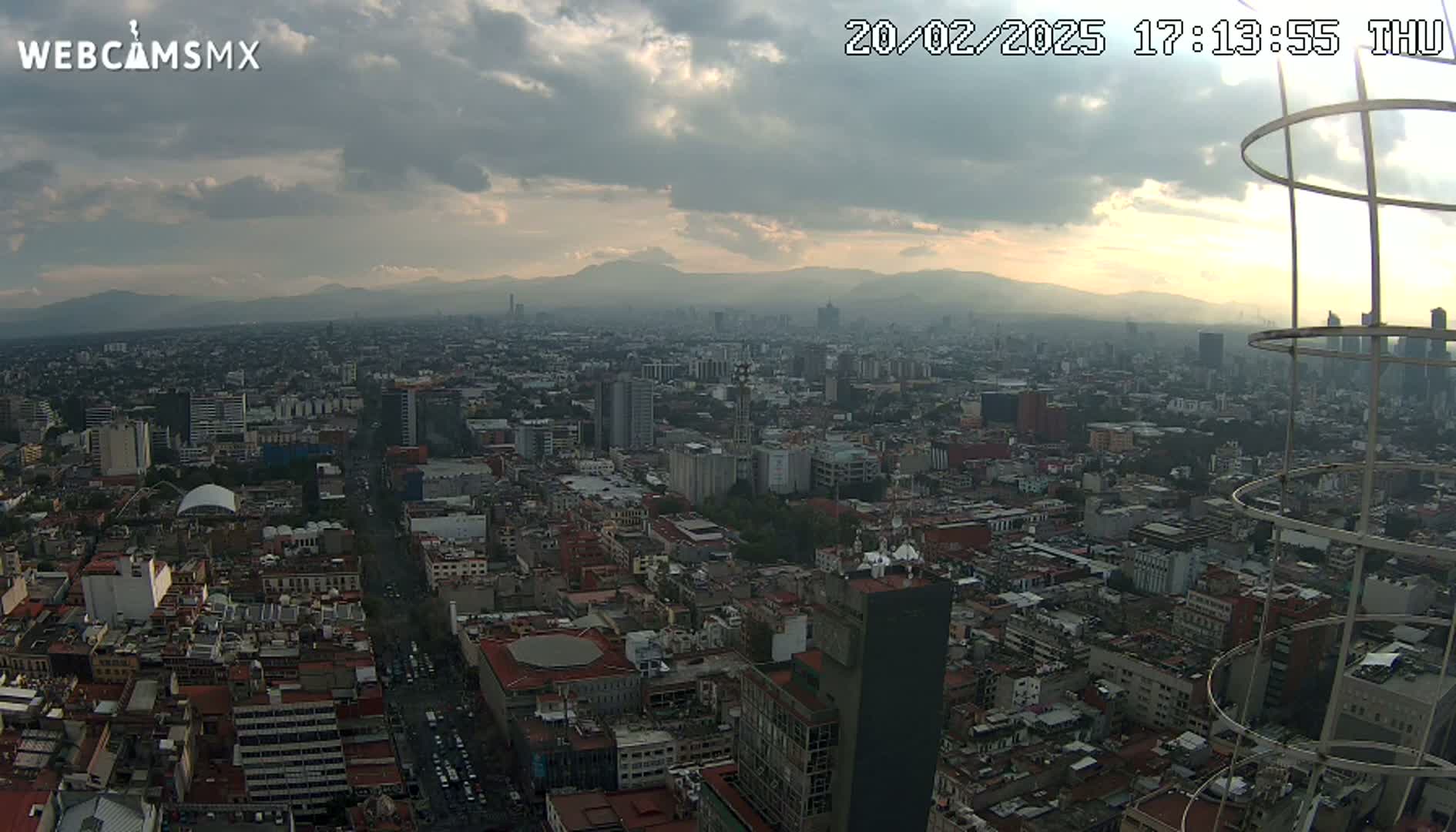 A sprawling cityscape under a partly cloudy sky, with mountains visible in the distance.